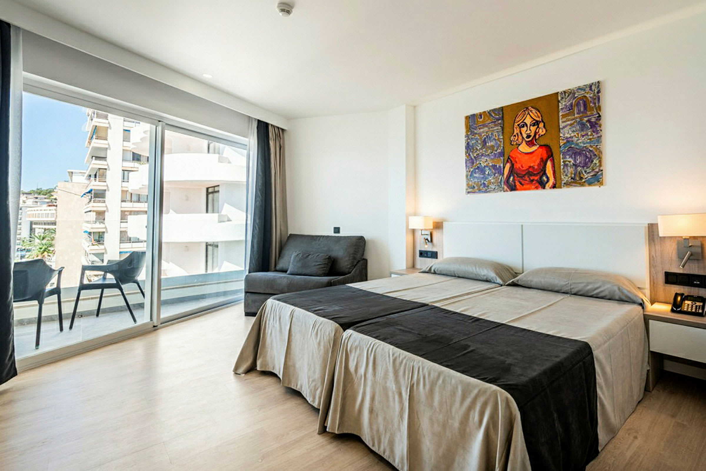 Ett hotellrum med två enkelsängar, en soffa, en balkong och stora glasfönster. (AI-genererad text)