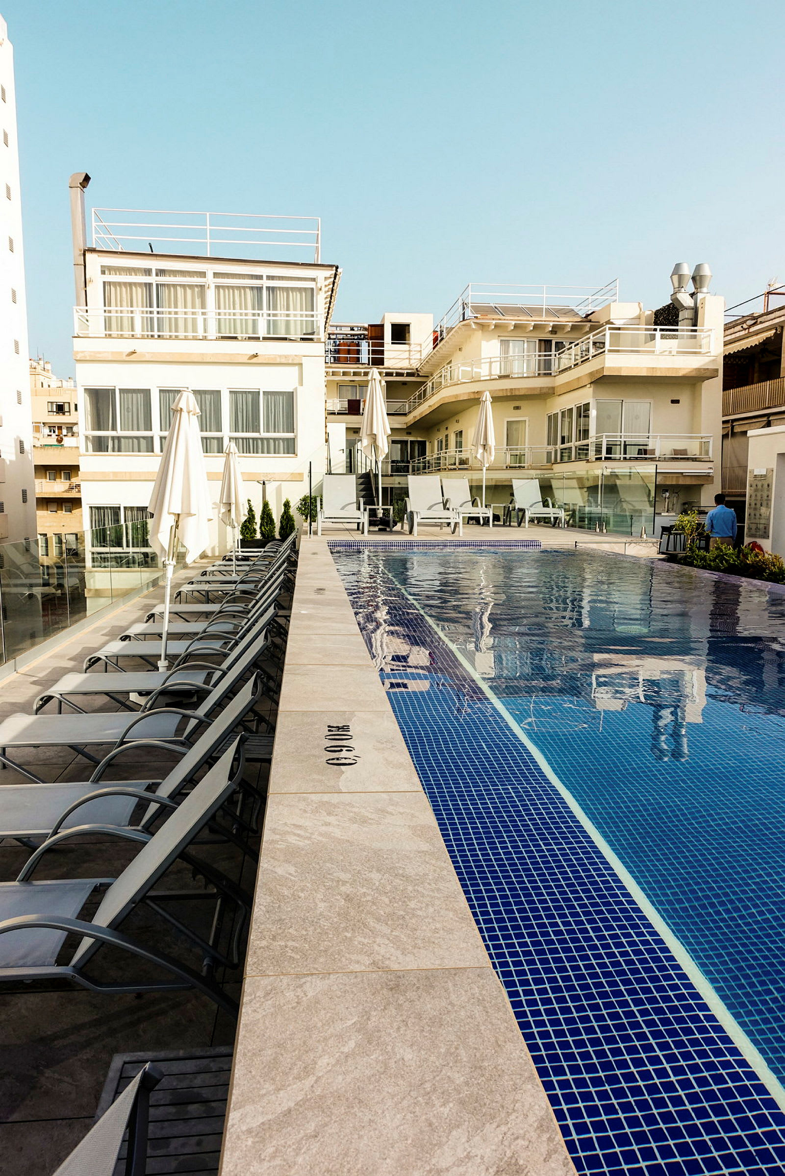 Ett poolområde vid ett hotell, med solstolar och parasoller uppställda längs poolen framför en byggnad. (AI-genererad text)