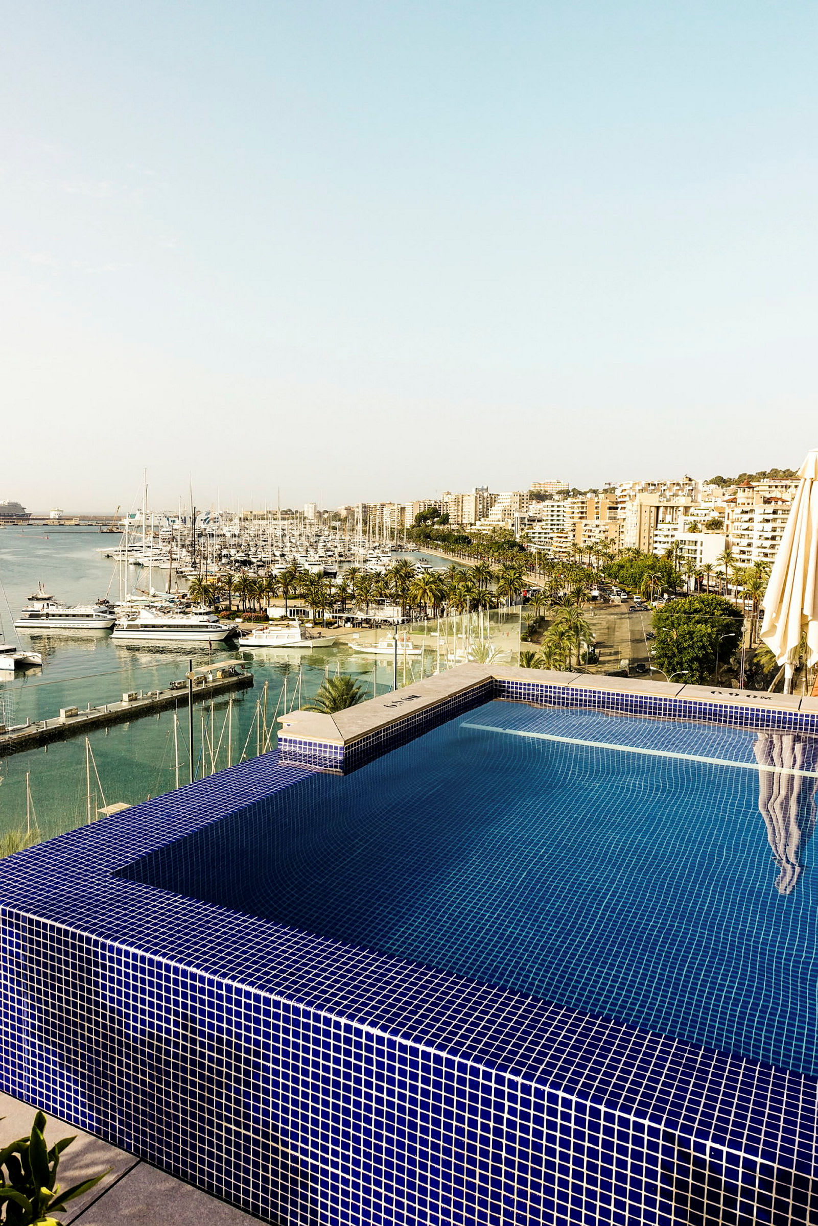 En utsikt över en infinitypool med blå mosaik, och en marina med båtar samt en stad i bakgrunden. (AI-genererad text)