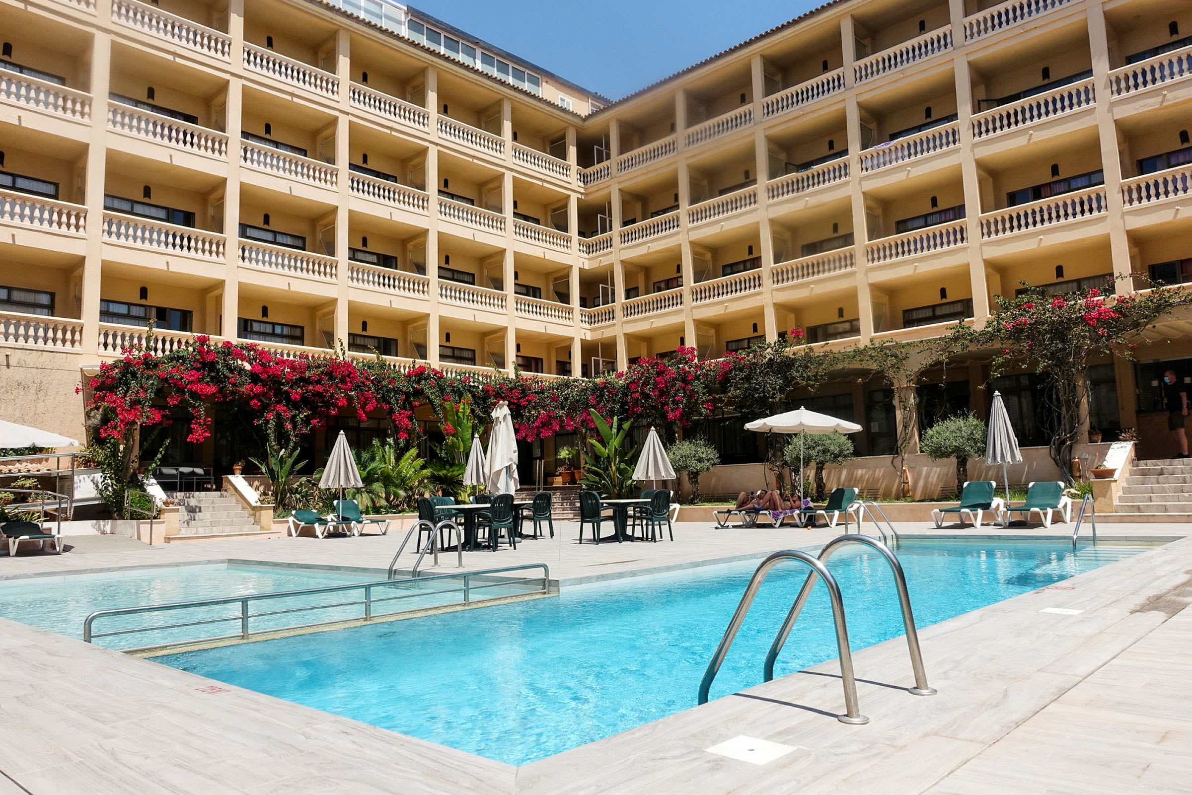 Bild på ett hotell med en utomhuspool och solstolar framför. (AI-genererad text)