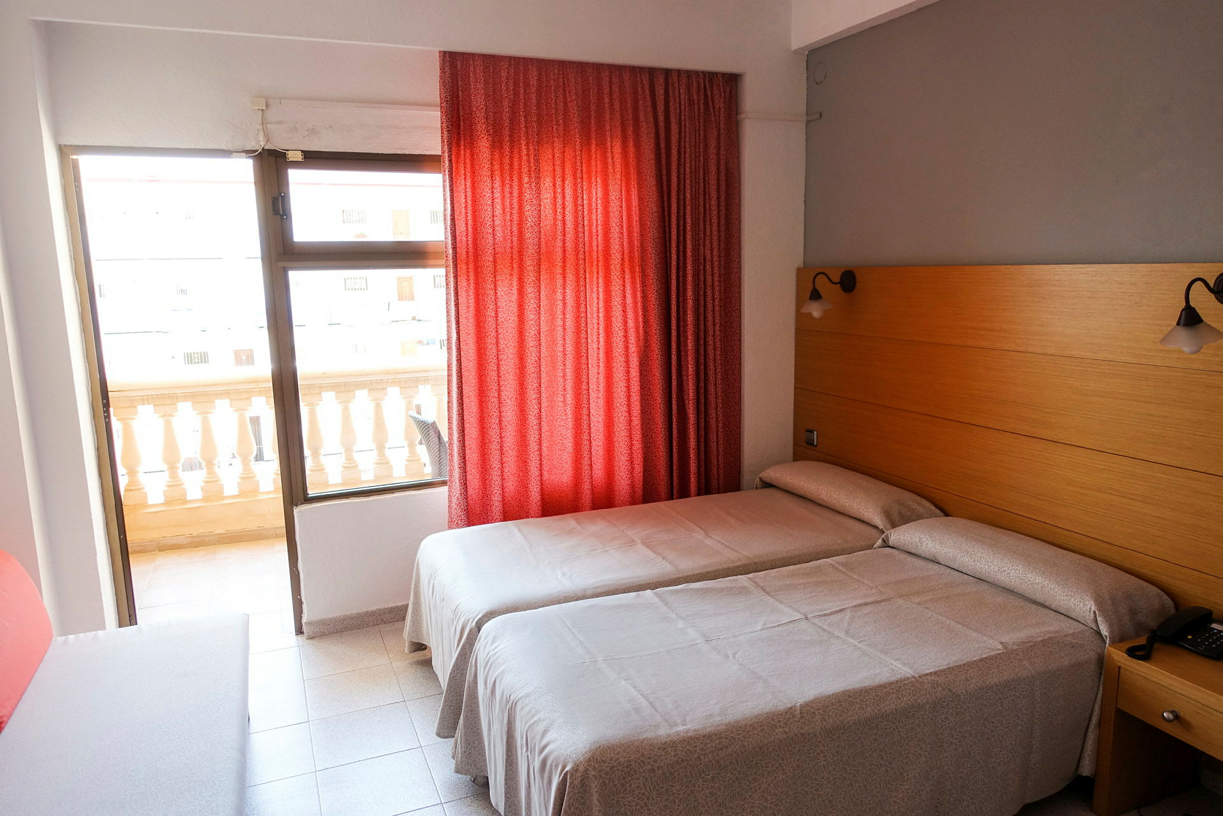 Hotellrum med två enkelsängar, röd gardin och balkong. (AI-genererad text)