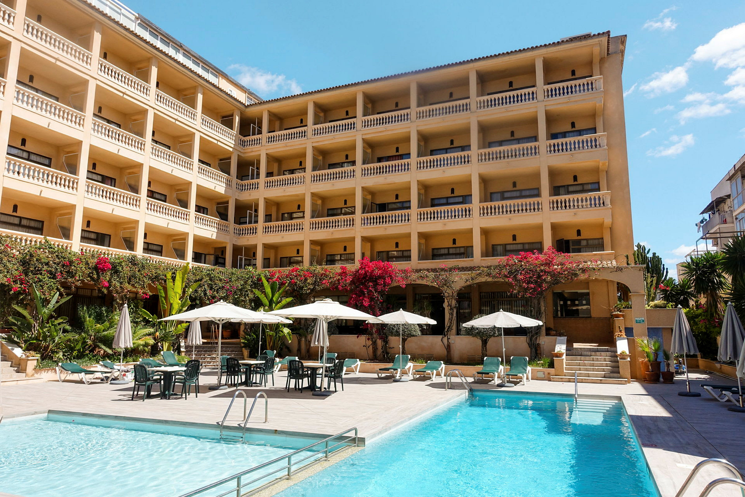 Hotell med flera våningar och balkonger, poolområde med solstolar och parasoll. (AI-genererad text)