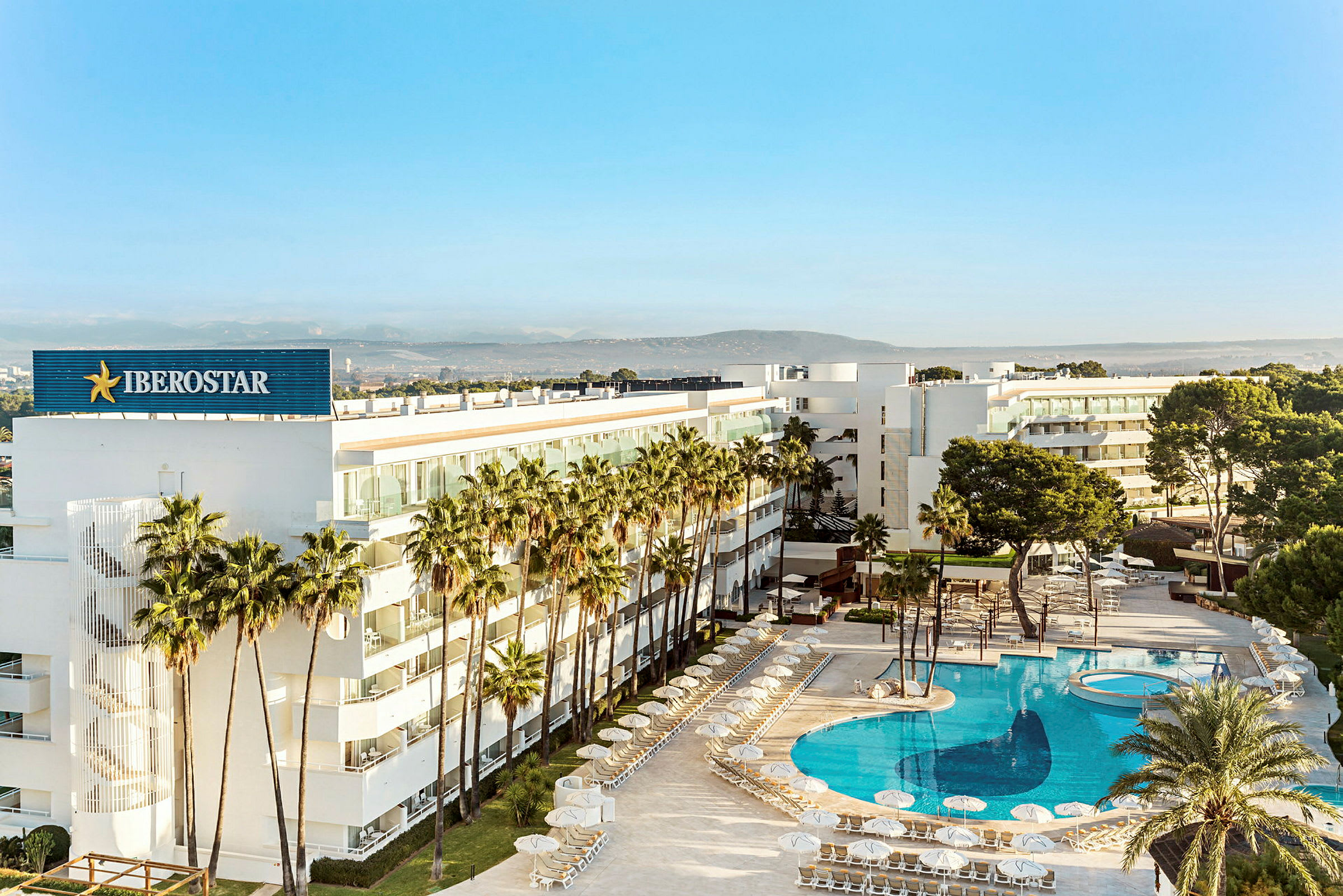 Ett modernt hotell omgärdat av palmer med en stor, klarblå pool. (AI-genererad text)