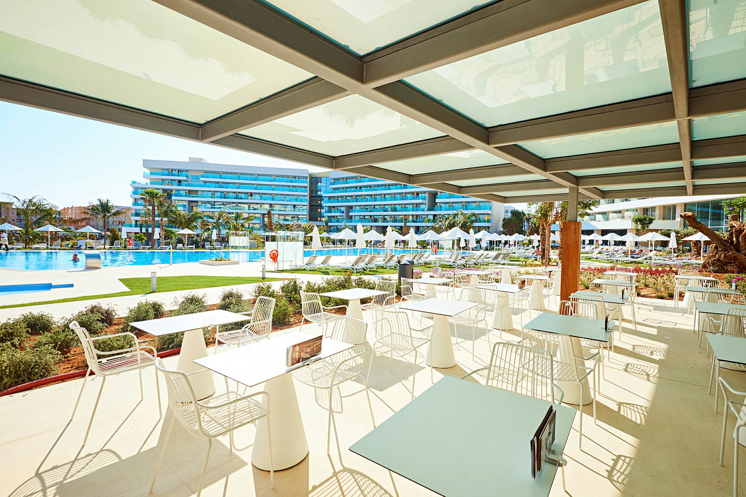 Utomhus sittplatser med utsikt över en pool och hotellbyggnader. (AI-genererad text)