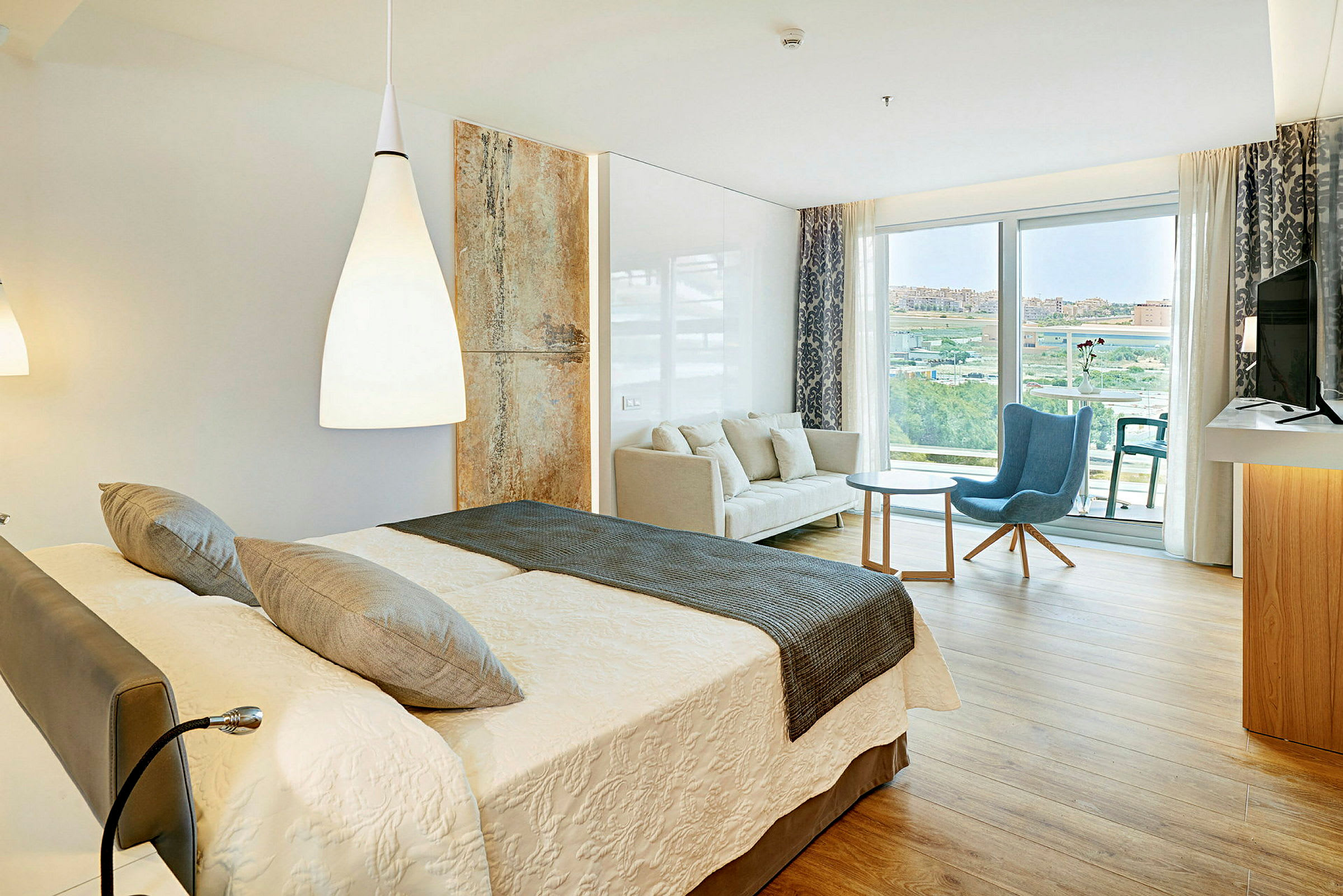 Ett hotellrum med en dubbelsäng, en soffa, en fåtölj och ett bord, samt en balkong med utsikt. (AI-genererad text)