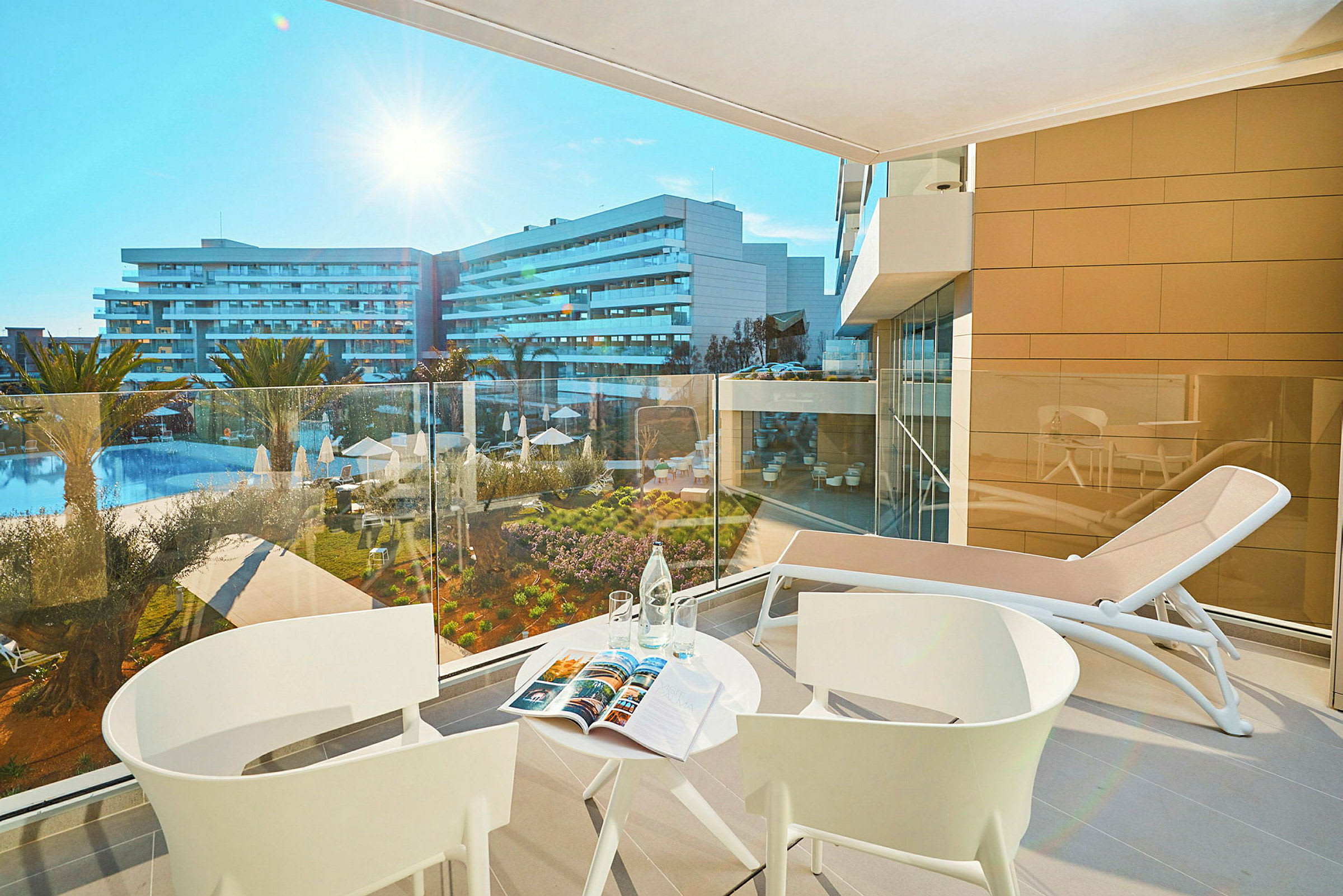 Utsikt från en balkong med bord och stolar mot ett hotellområde med pool. (AI-genererad text)