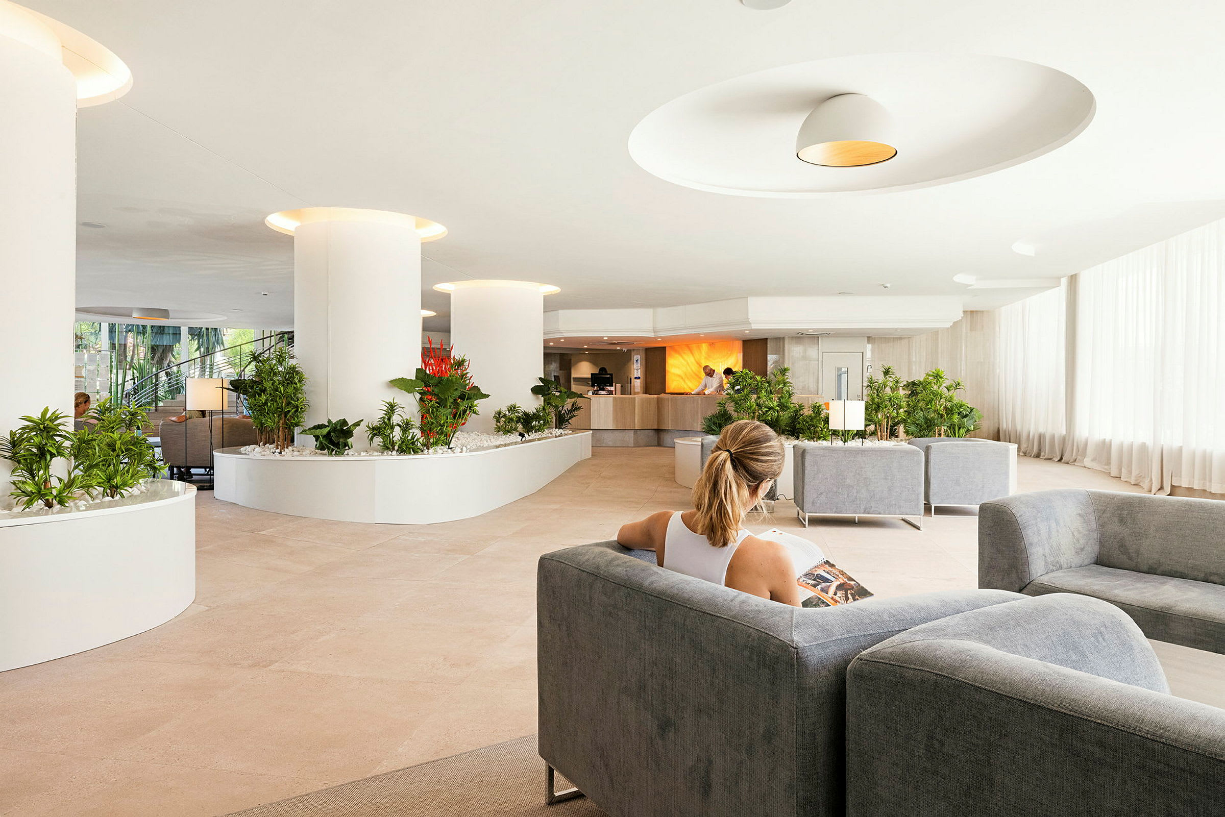 Person sitter i en rymlig hotellobby med modern inredning och grönska. (AI-genererad text)