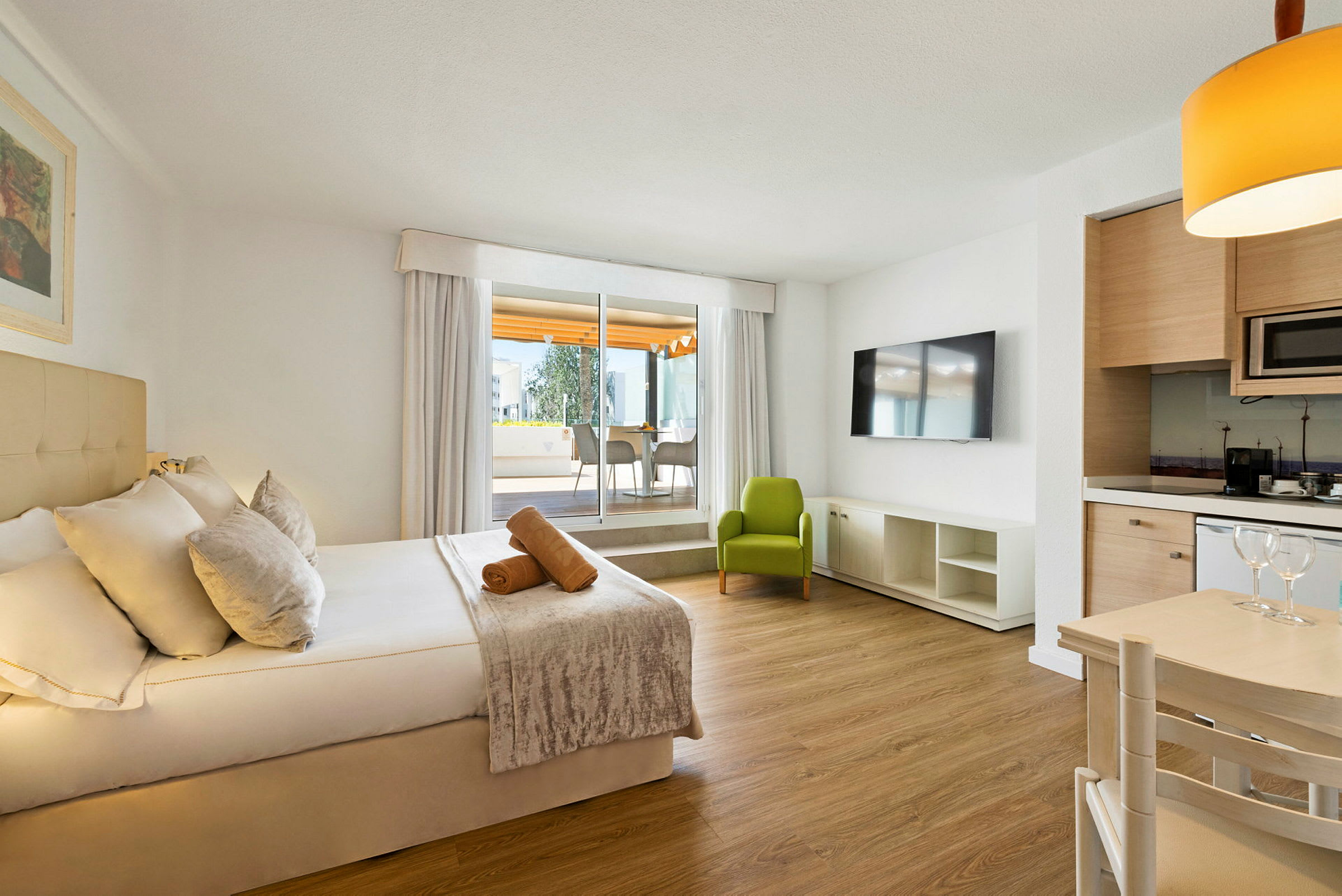 Ett modernt hotellrum med en dubbelsäng, ett grönt fåtölj, en TV, samt ett bord och köksyta. (AI-genererad text)