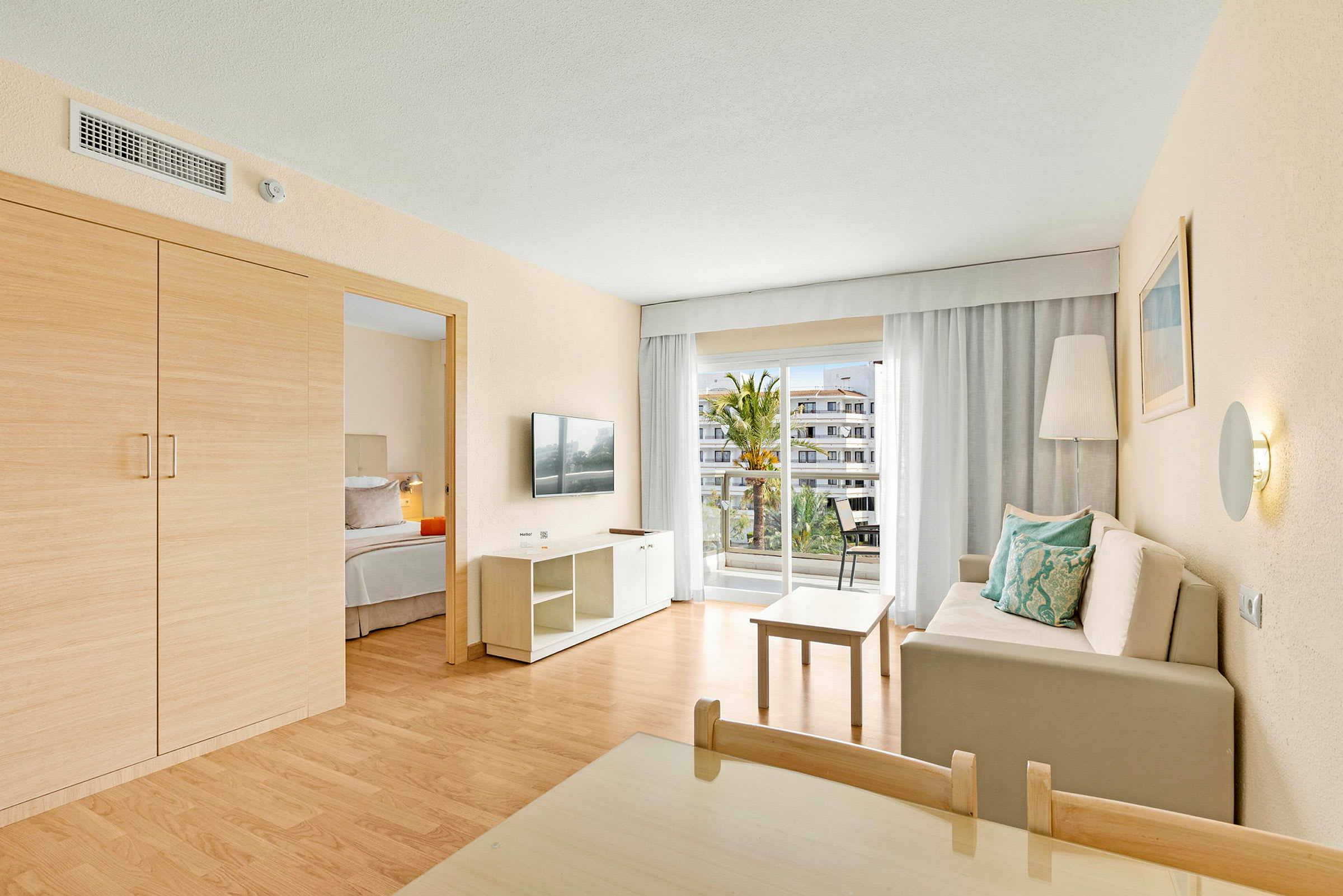 Ett hotellrum med ett vardagsrum, en soffa med kuddar, ett bord, en tv och en balkong med utsikt. (AI-genererad text)