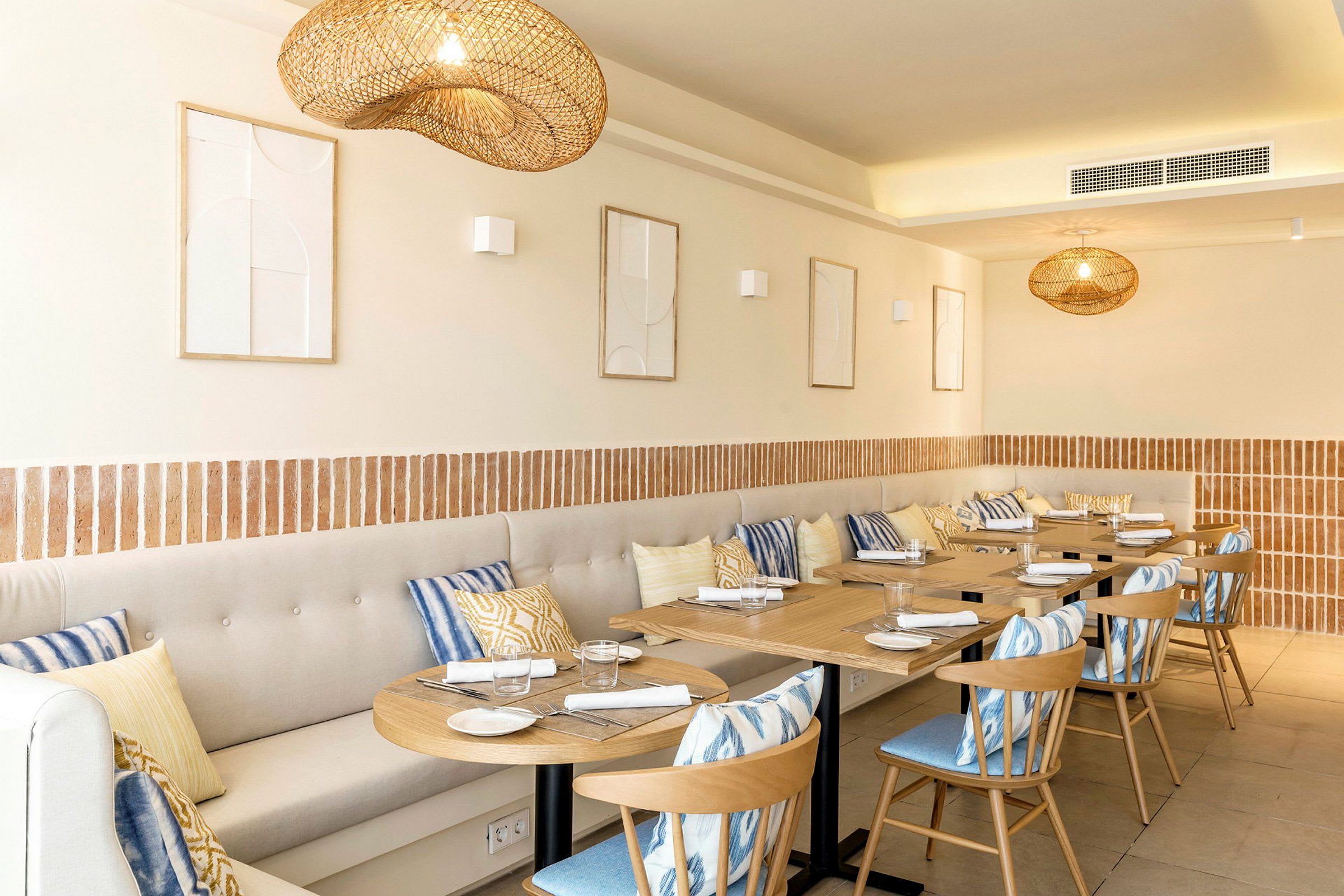 En restaurang med träbord, stolar och beige sittbänkar dekorerade med färgglada kuddar. (AI-genererad text)