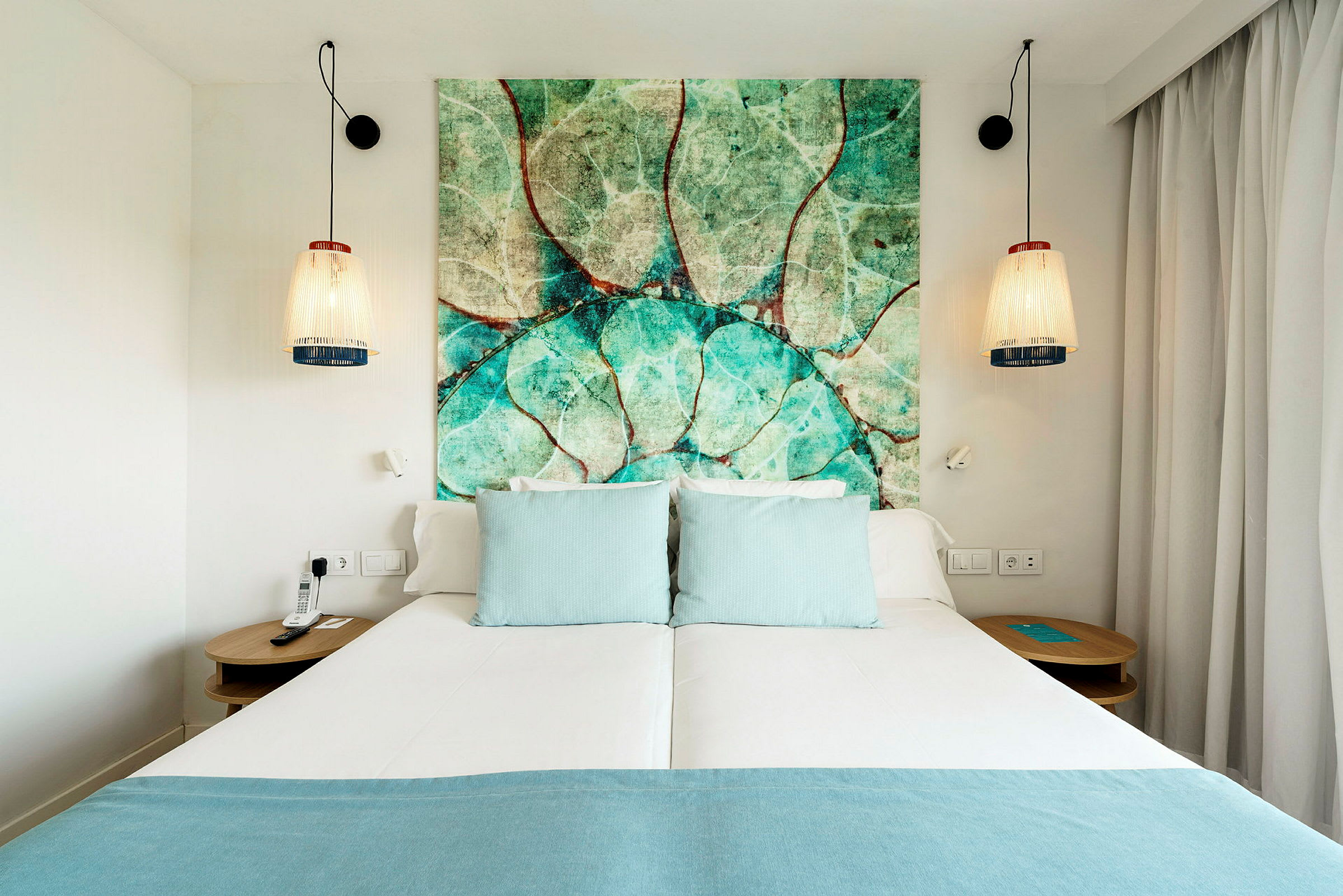 Hotellsäng med turkosa kuddar och ett huvudgavel med naturmotiv. (AI-genererad text)