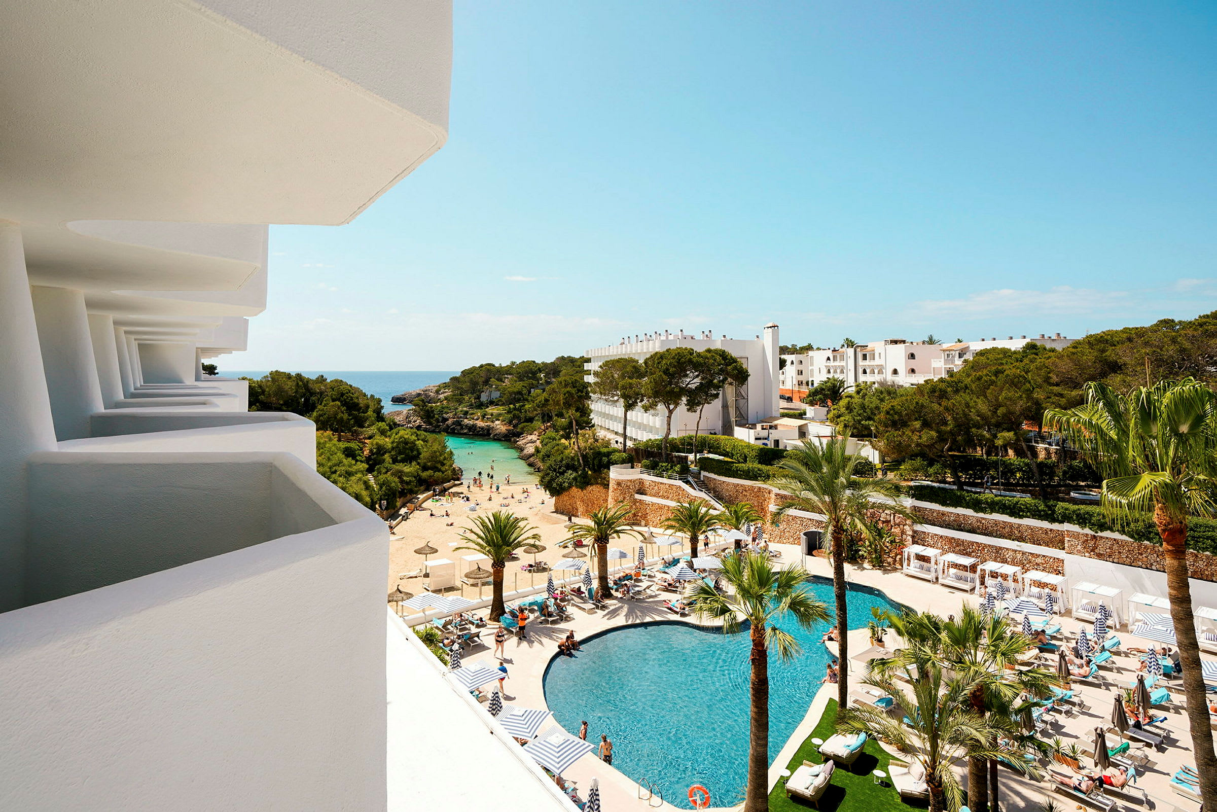 Utsikt från en balkong mot ett hotellområde med pool, strand och träd. (AI-genererad text)