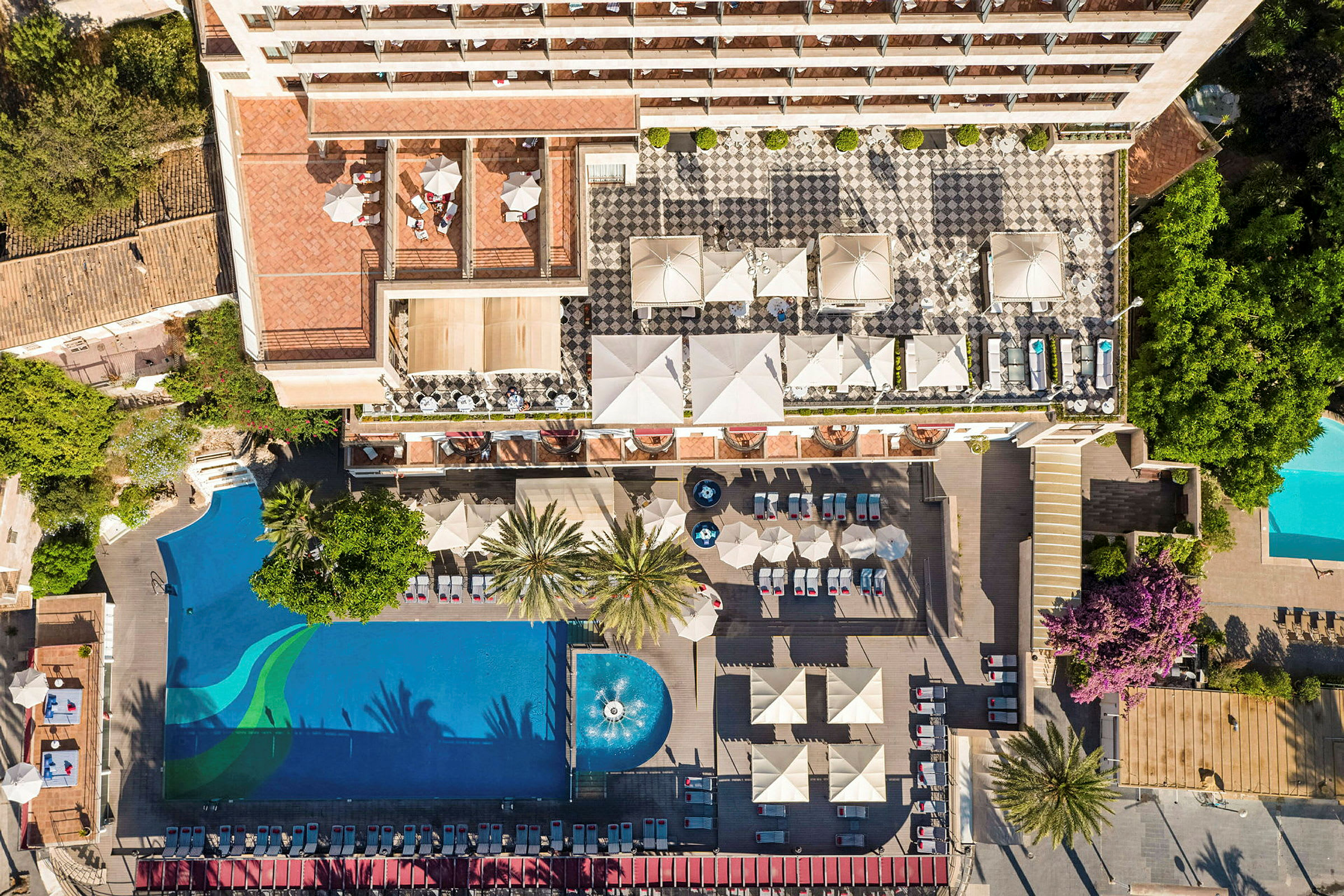 Drönarbild av en hotellanläggning med en pool, solstolar, parasoller och en uteplats. (AI-genererad text)