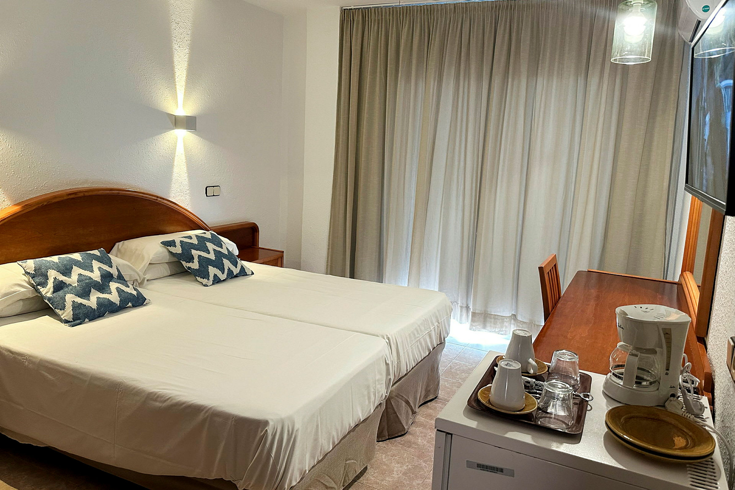 Ett hotellrum med två enkelsängar, en skrivbordsyta, och en kaffemaskin. (AI-genererad text)