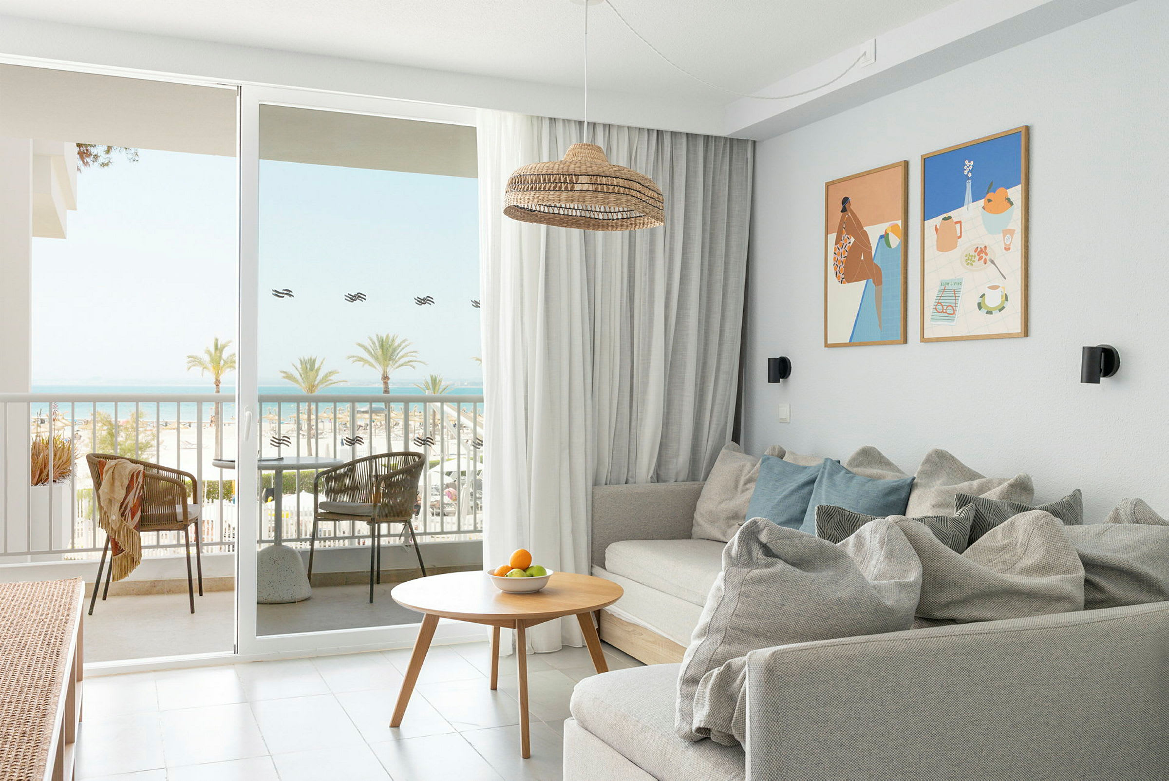 En ljus och modern hotellrumsvistelse med en soffa, soffbord och dörrar som öppnar sig mot en balkong med havsutsikt. (AI-genererad text)