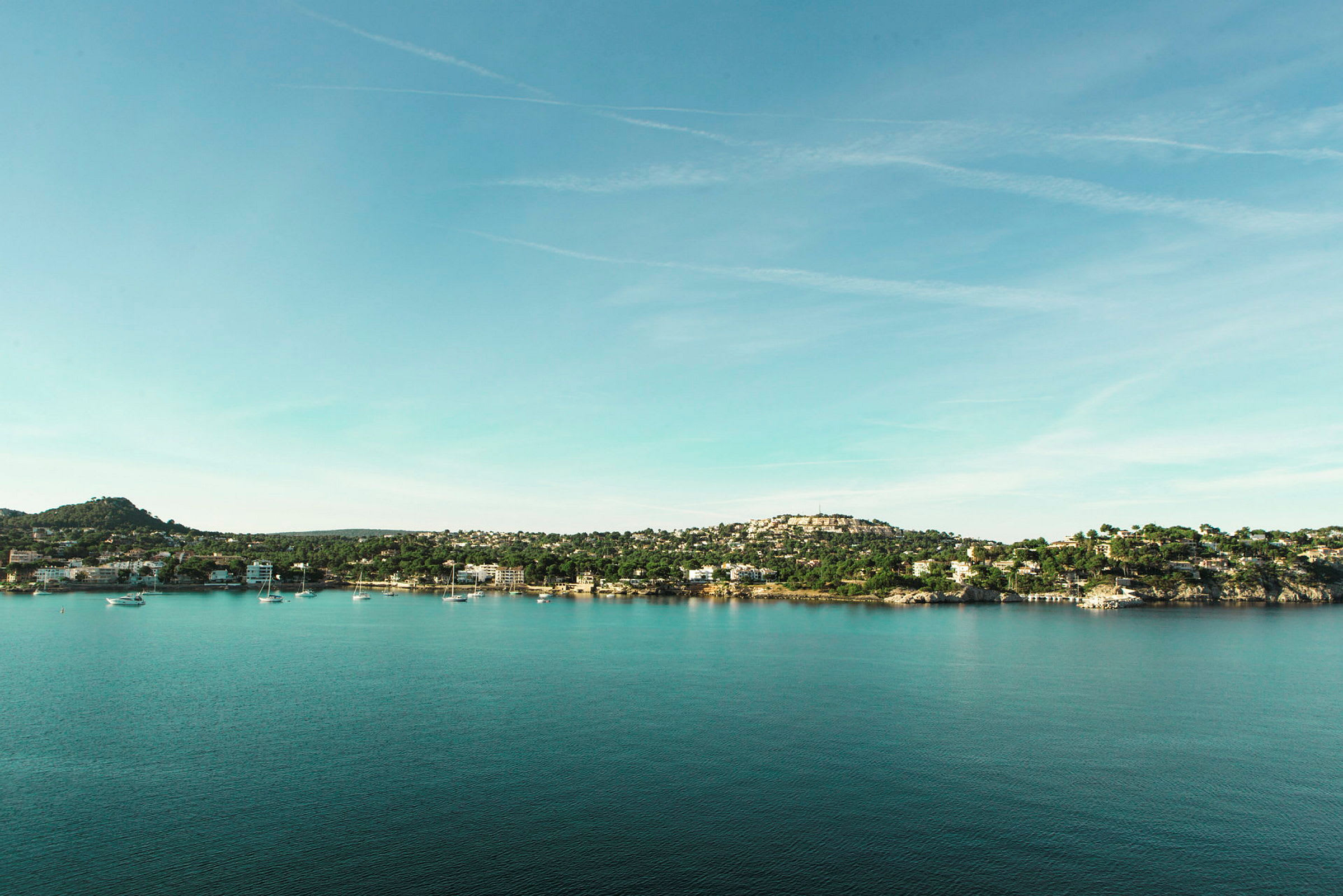 Vy över en kustlinje med hus och båtar vid vattnet under en klar himmel. (AI-genererad text)