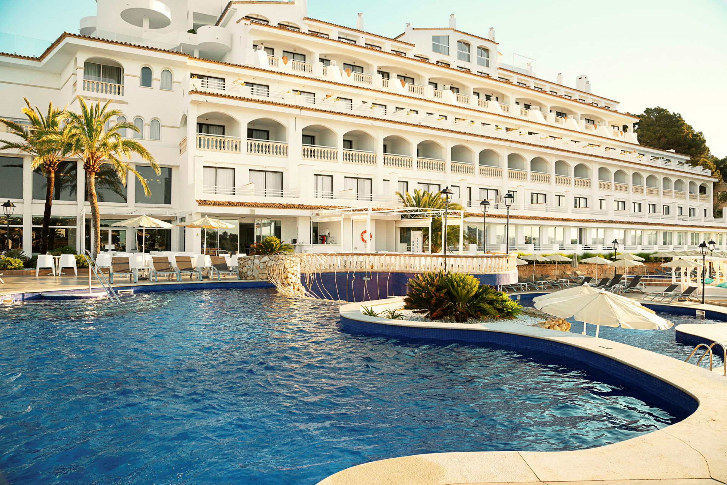 Hotell med vit fasad och swimmingpool i förgrunden. (AI-genererad text)