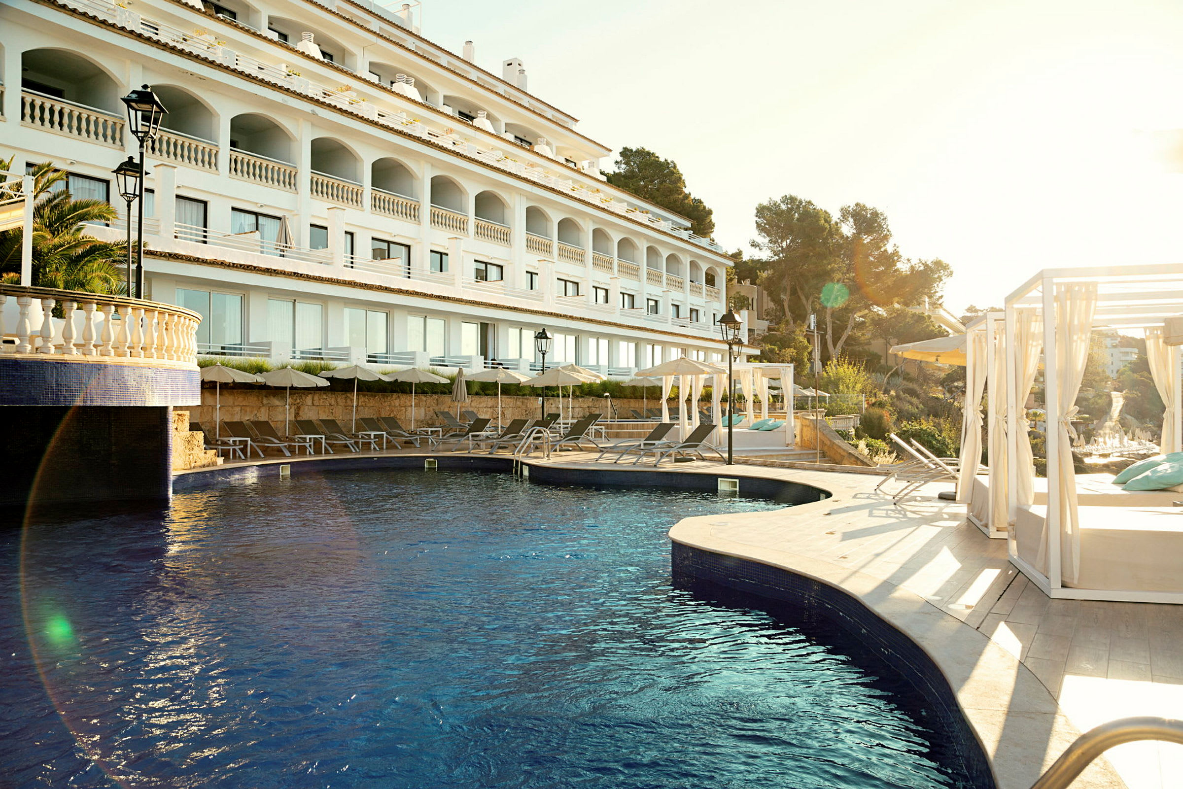 En modern hotellbyggnad med en utomhuspool och solstolar under parasoller. (AI-genererad text)