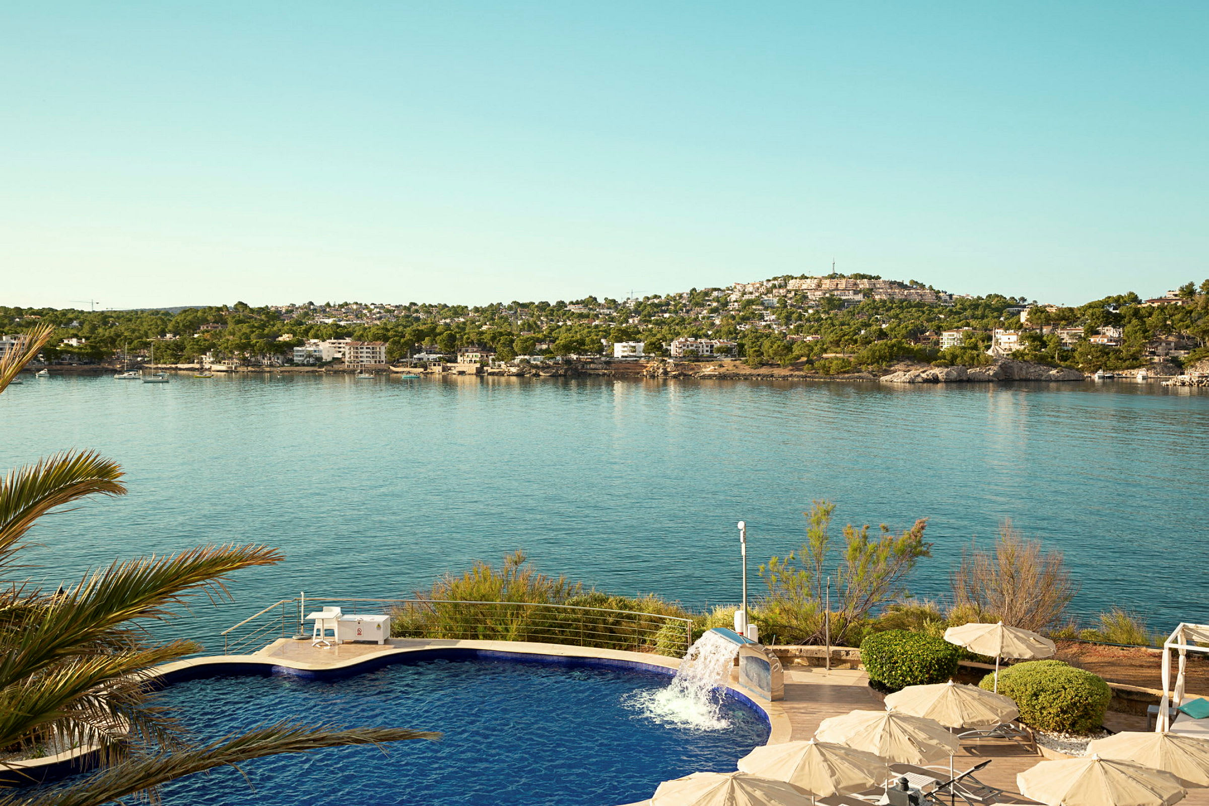 En pool med en fontän framför havet och en bergig kustlinje. (AI-genererad text)