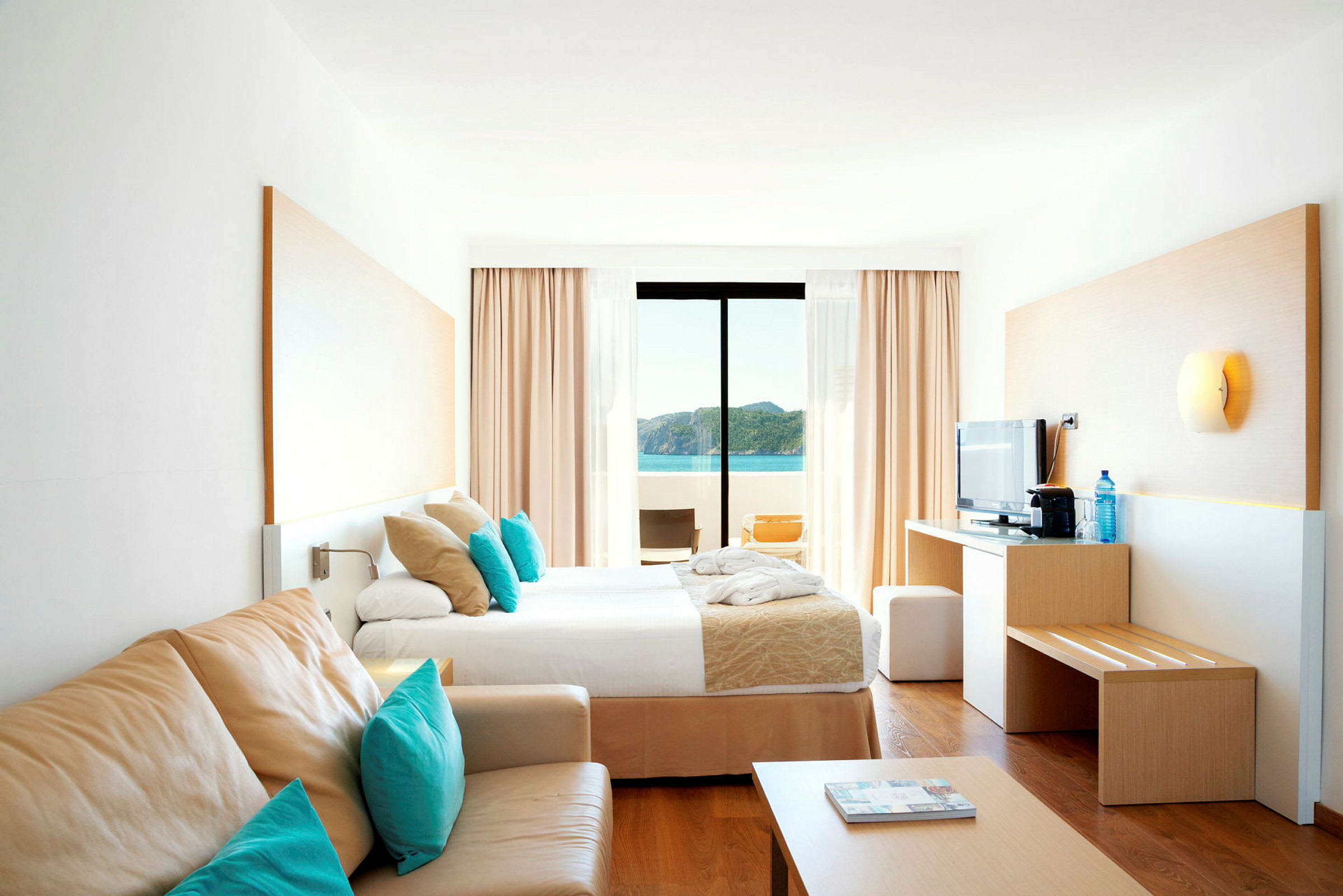 Ett ljust hotellrum med en säng, soffa och utsikt över havet. (AI-genererad text)