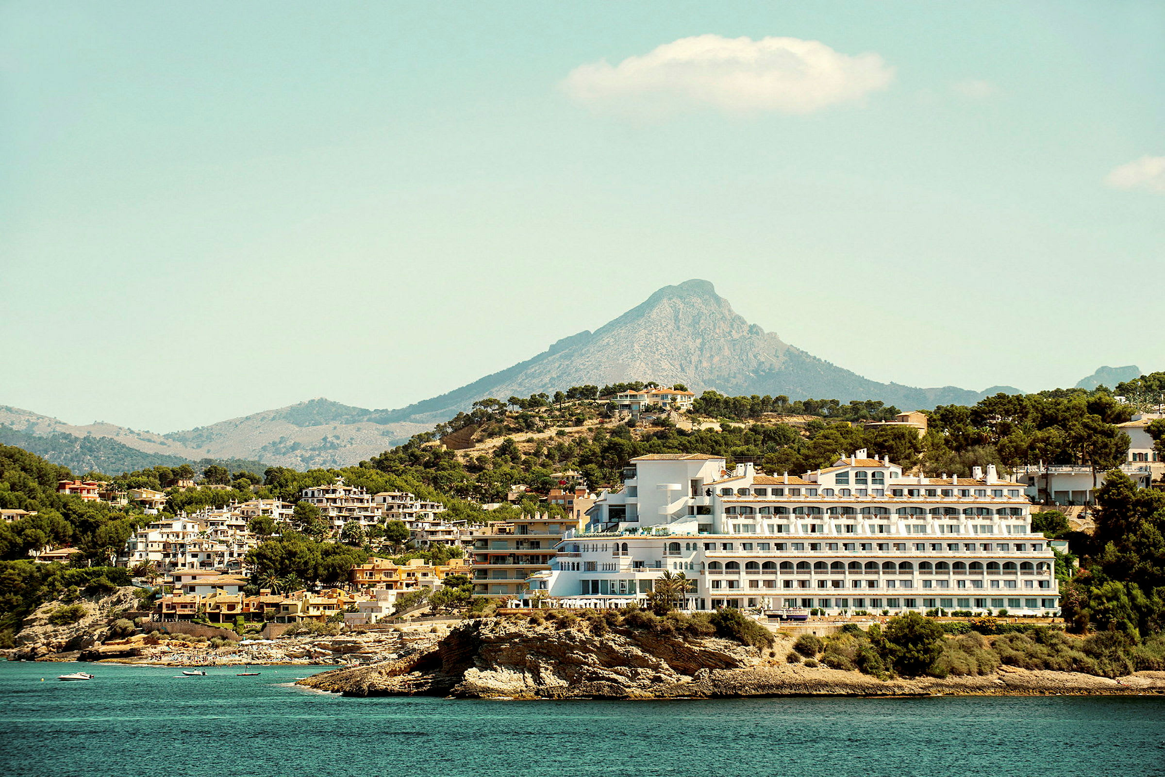 Bild av en hotellbyggnad vid kusten med berg i bakgrunden. (AI-genererad text)
