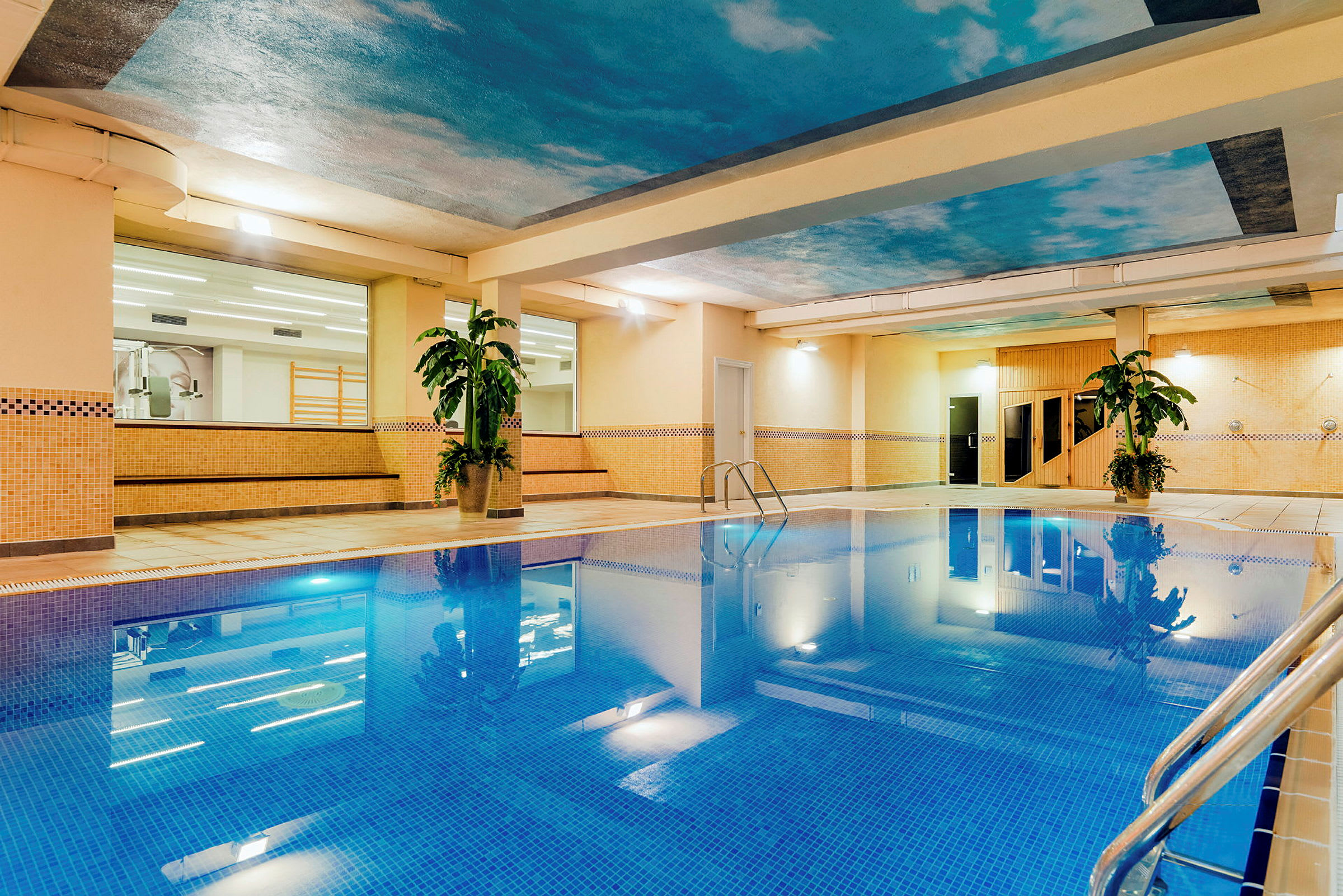 Inomhuspool med mosaikplattor, omgiven av beige väggar och dekorativa växter. (AI-genererad text)