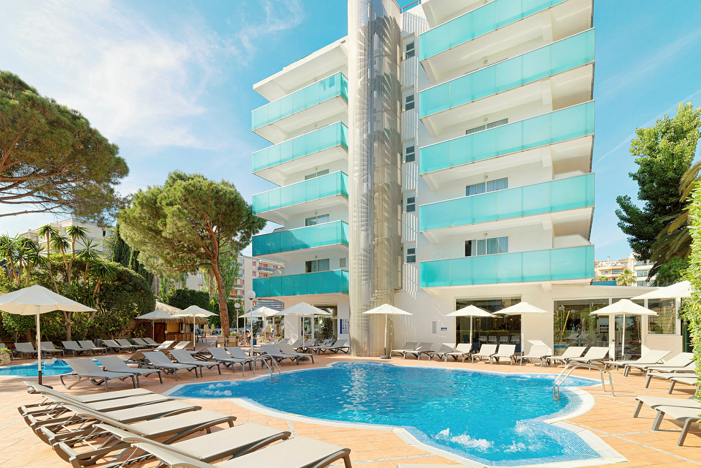 Flerfamiljshus med balkonger i turkost glas vid en rund swimmingpool omgiven av solstolar och parasoller. (AI-genererad text)