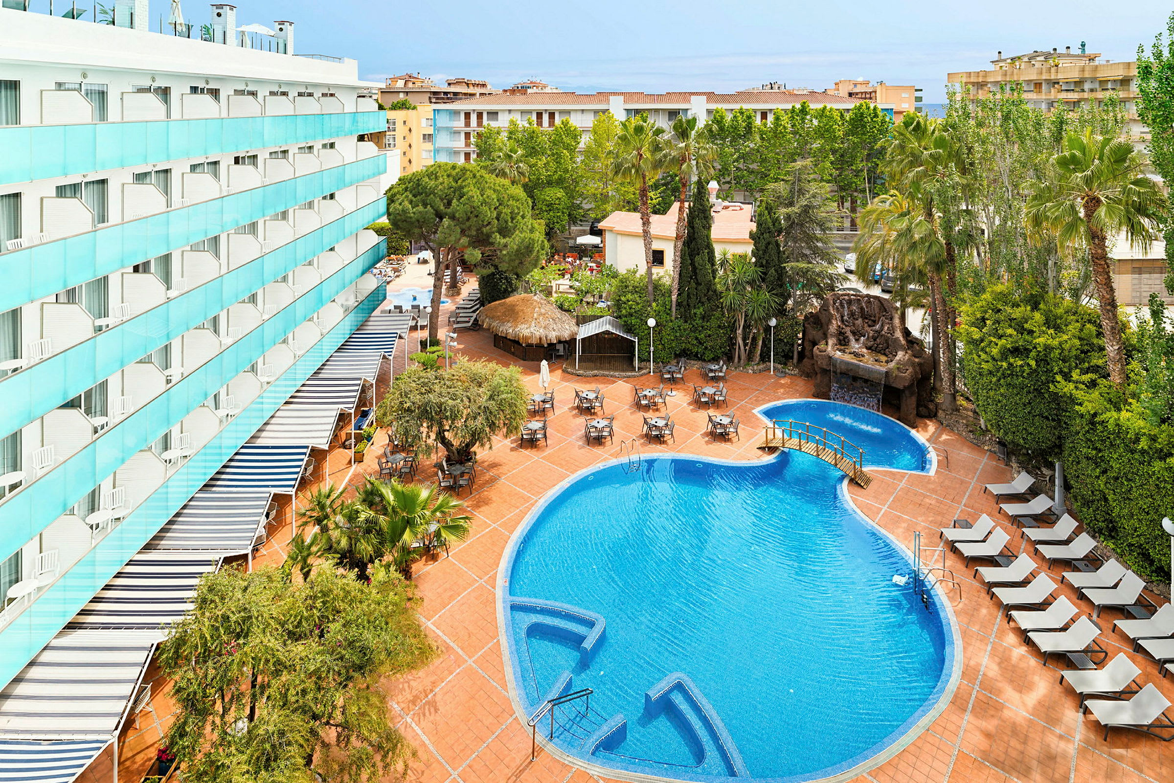 Utomhusområde med pool, solstolar och bord samt hotellbyggnad i bakgrunden. (AI-genererad text)