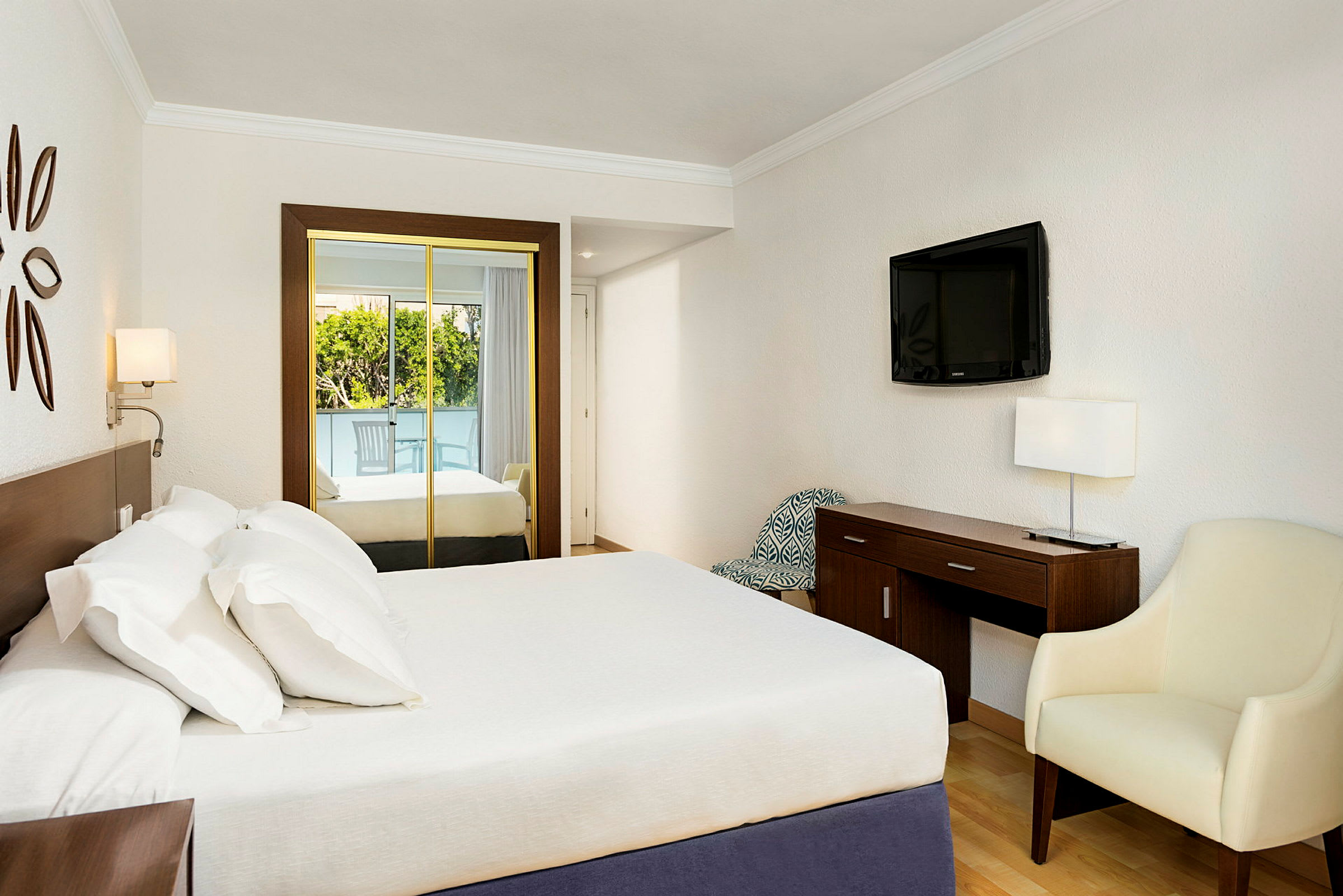 Ett hotellrum med en dubbelsäng, spegelskåp, en TV på väggen och en skrivbordshörna med en stol. (AI-genererad text)