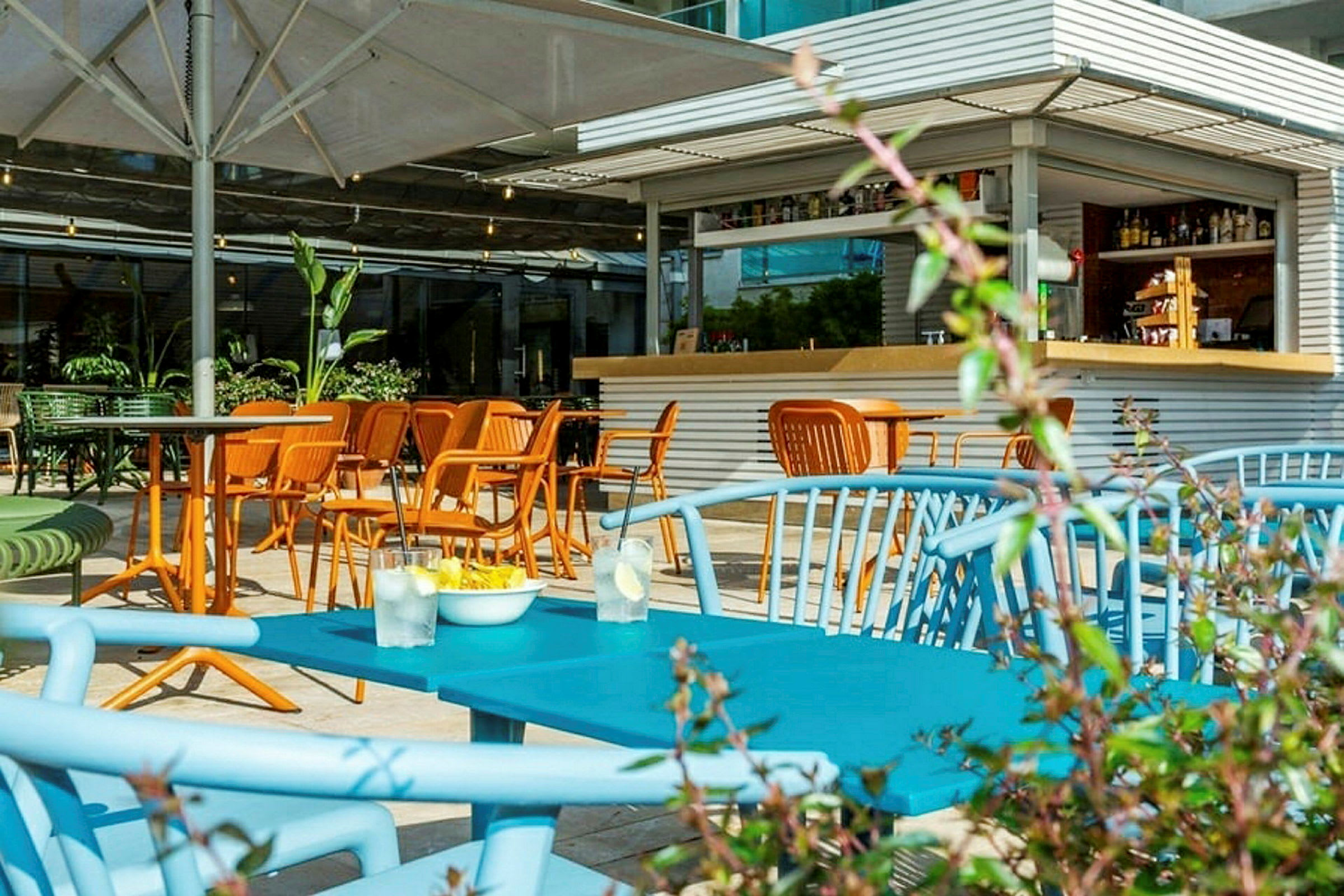 Bild av en uteservering med färgglada stolar och bord, samt en liten bar bakom. (AI-genererad text)
