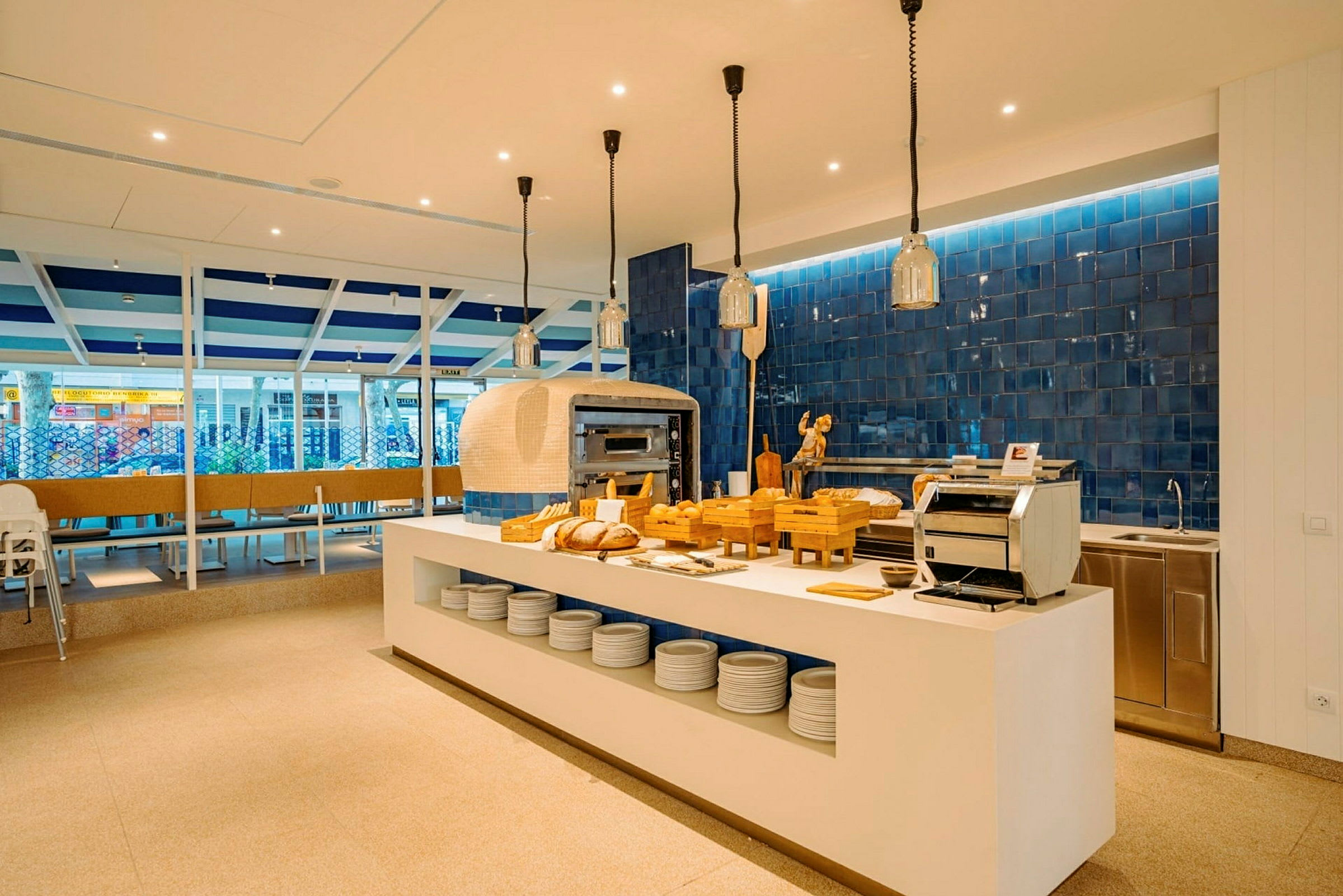 En modern restaurangmiljö med ett öppet kök och matbord i fokus. Bröd och köksutrustning finns på en vit bänk. (AI-genererad text)