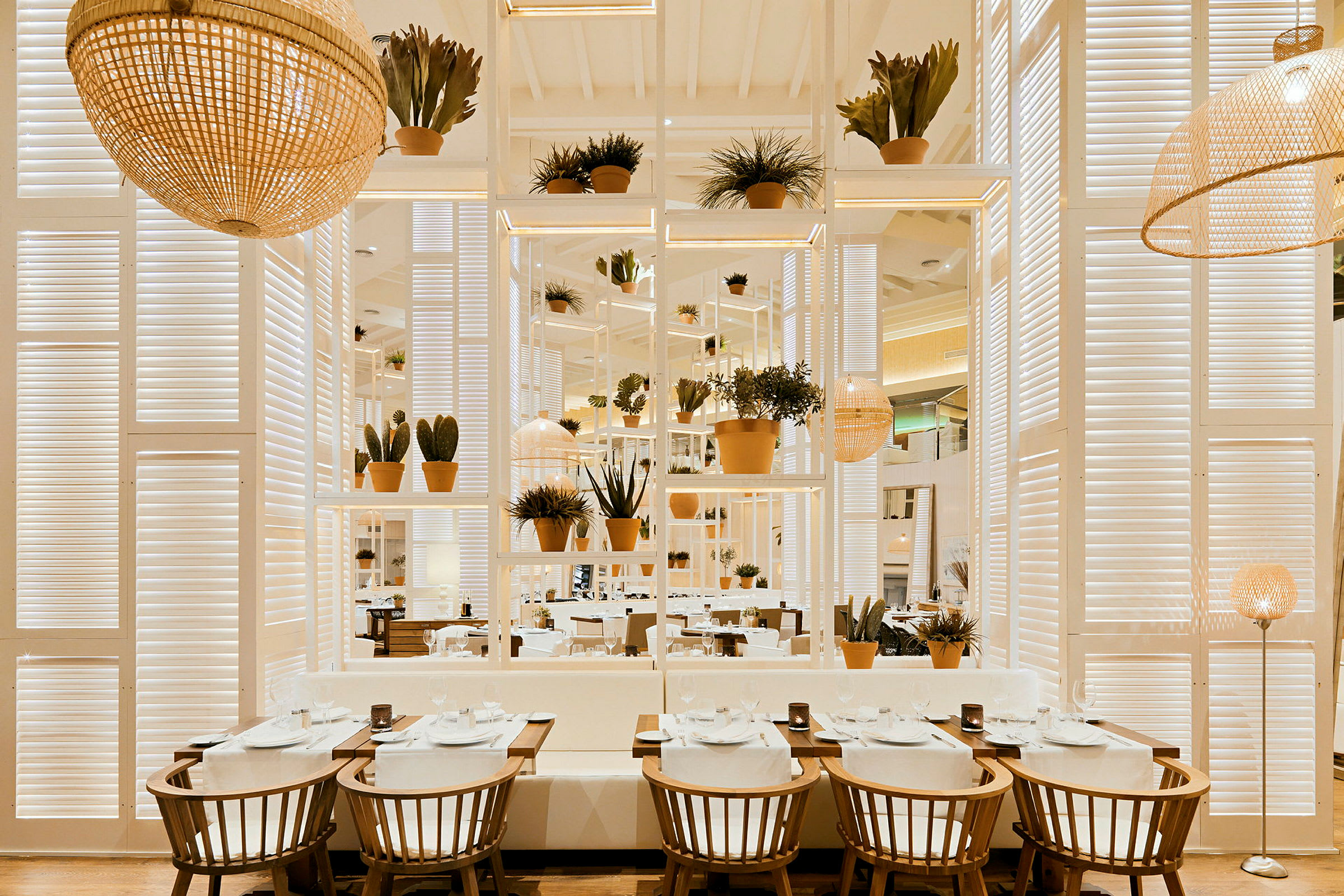 Interiör av en restaurang med bord, stolar och växter i en ljus och modern design. (AI-genererad text)