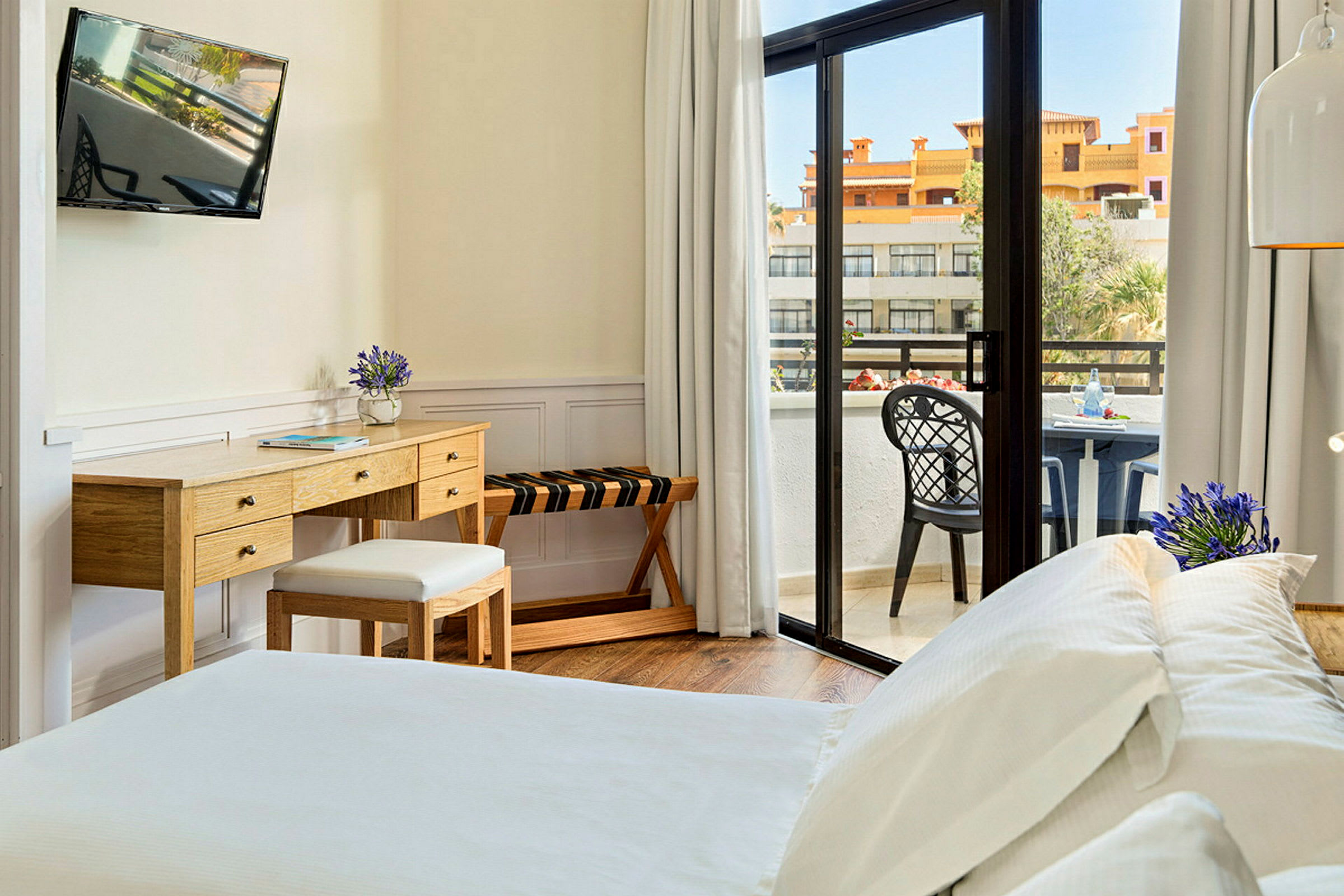 Ett hotellrum med en säng, skrivbord och en balkong med utsikt. (AI-genererad text)