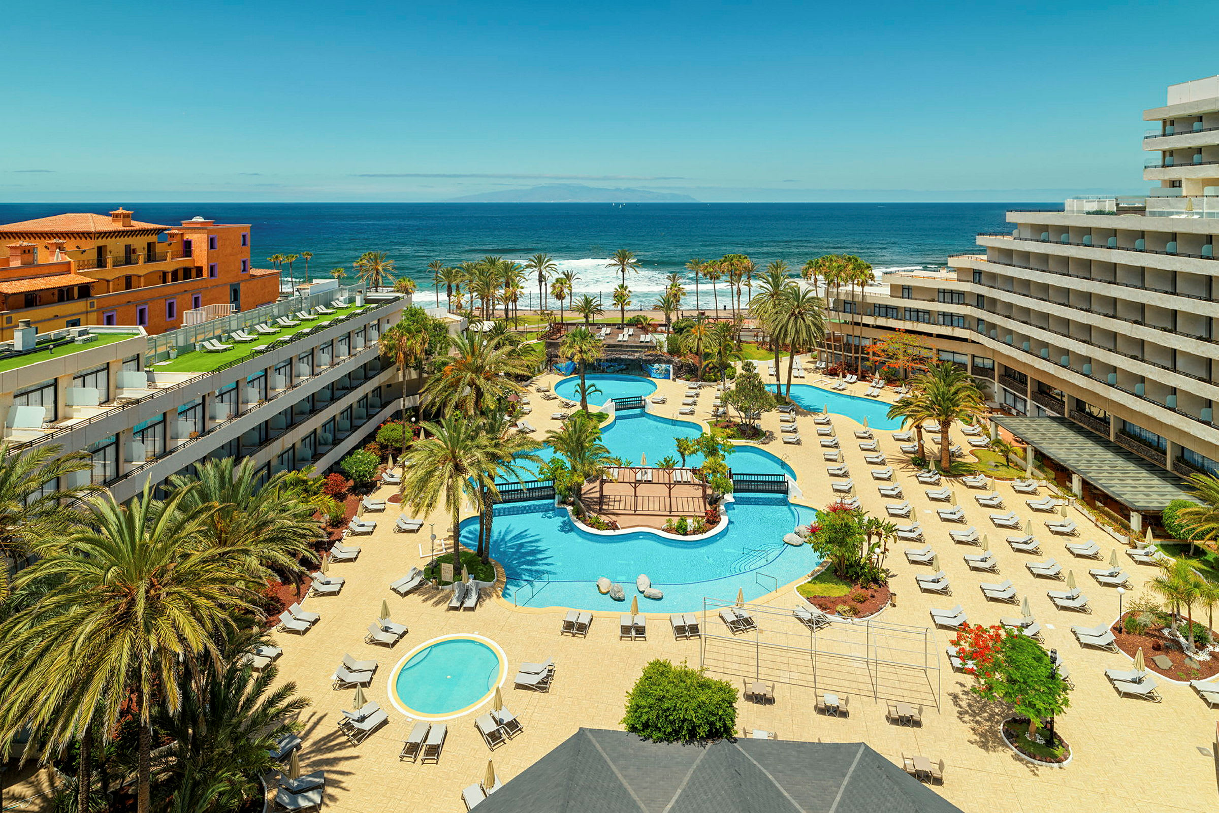 En hotellanläggning med pooler, solstolar och palmer, nära havet. (AI-genererad text)
