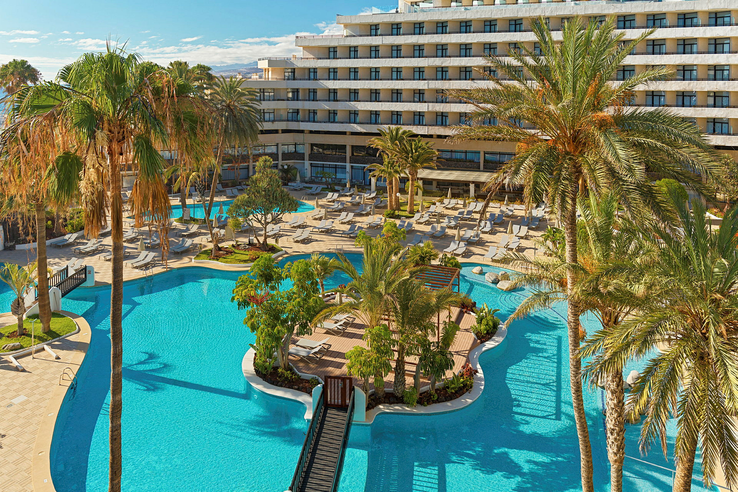 En stor pool med omgivande palmer och en hotellbyggnad i bakgrunden. (AI-genererad text)