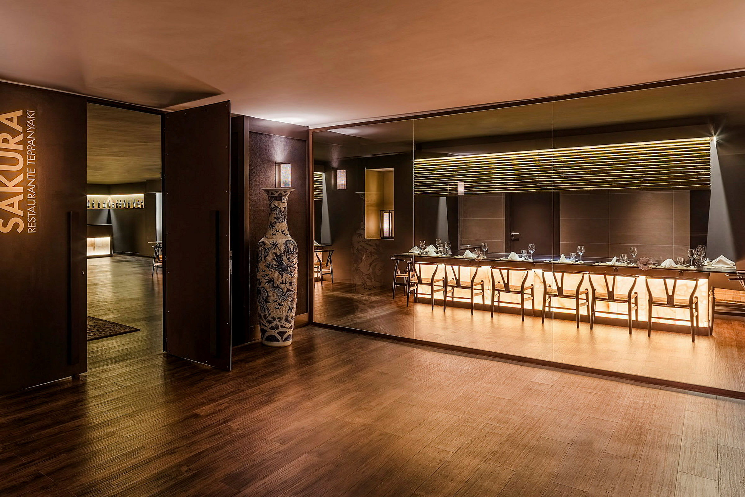 En elegant restaurang med modern inredning, ett stort bord och stolar framför en belyst vägg. (AI-genererad text)