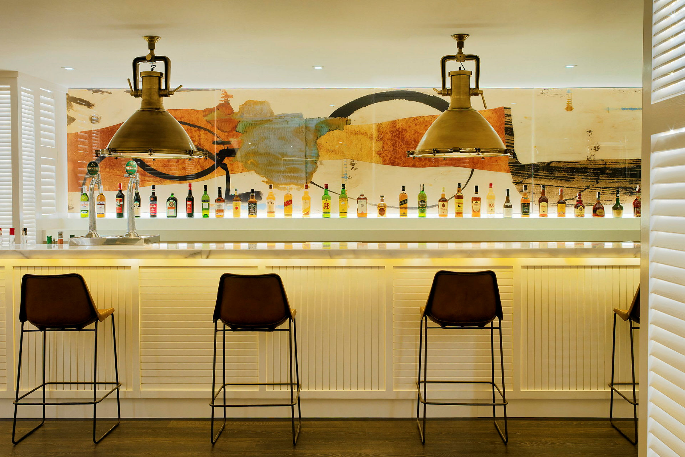Bild av en modern bar med stolar och flaskor uppradade på bardisken inför en färgrik bakgrund. (AI-genererad text)