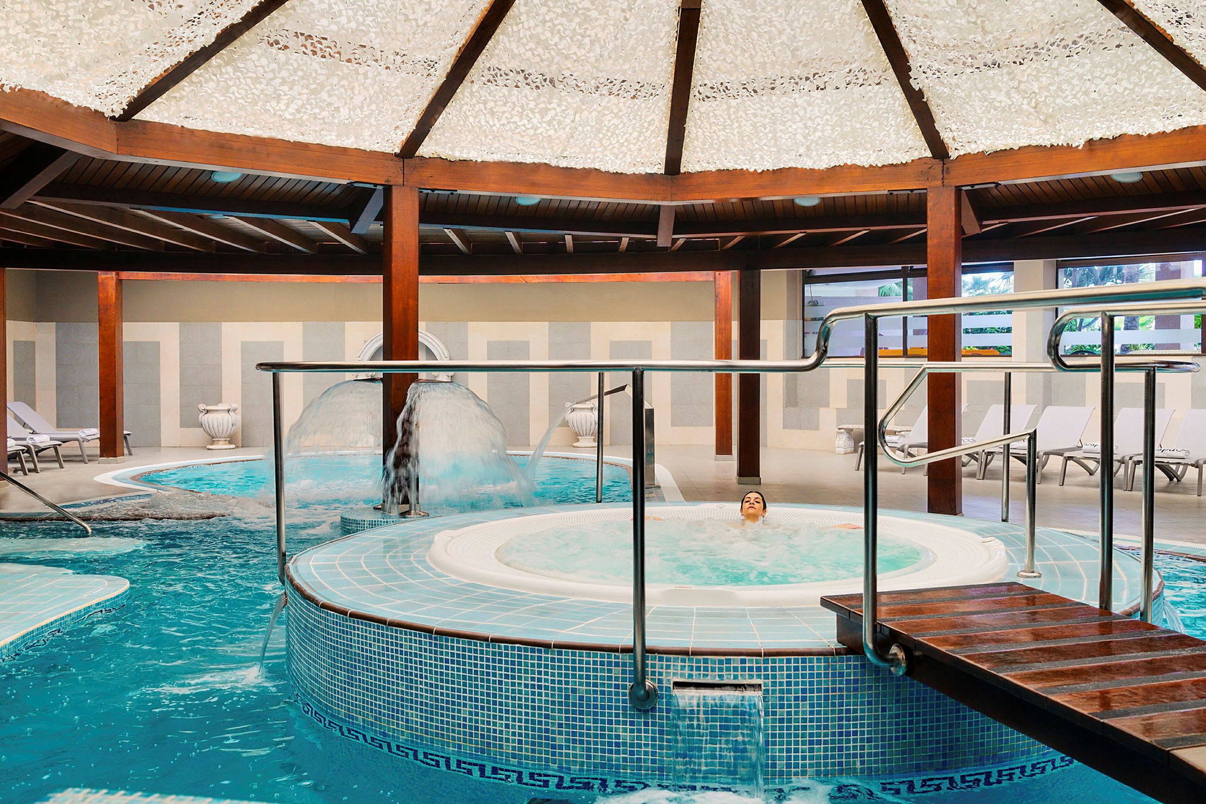 Interiör av ett spa med pool, jacuzzi och bekväma solstolar. (AI-genererad text)