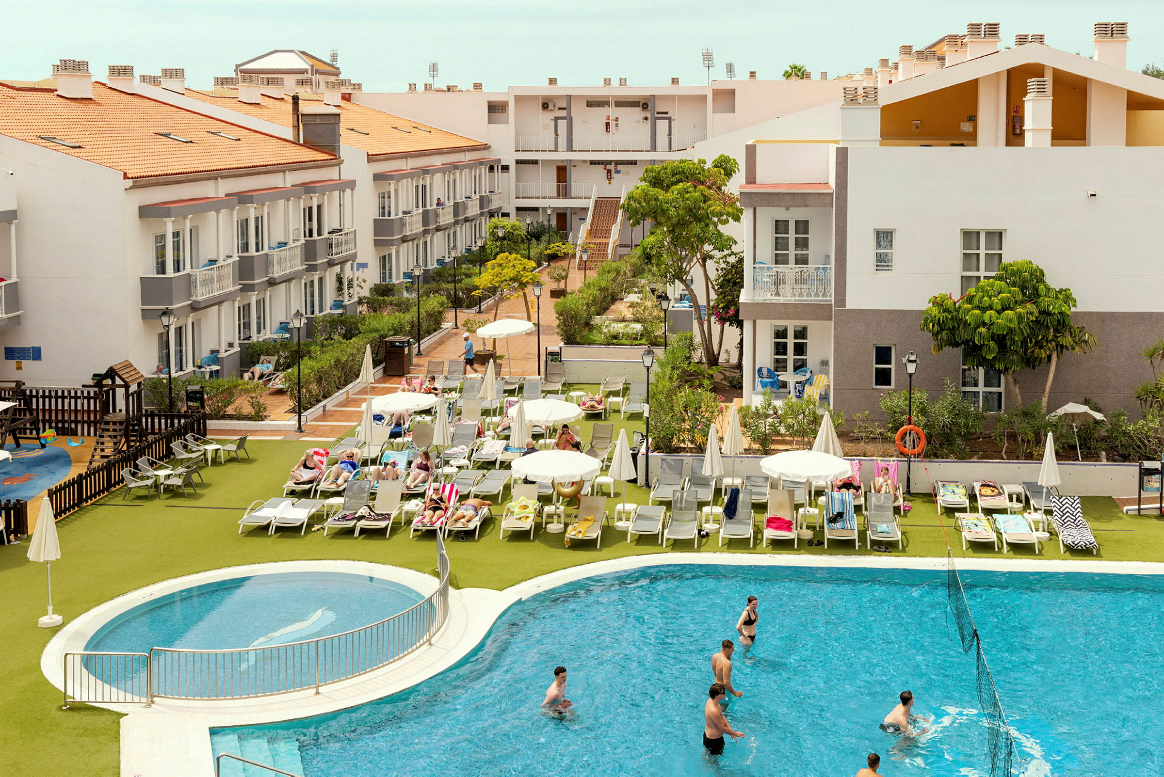 Hotellområde med byggnader, solstolar och en pool. (AI-genererad text)