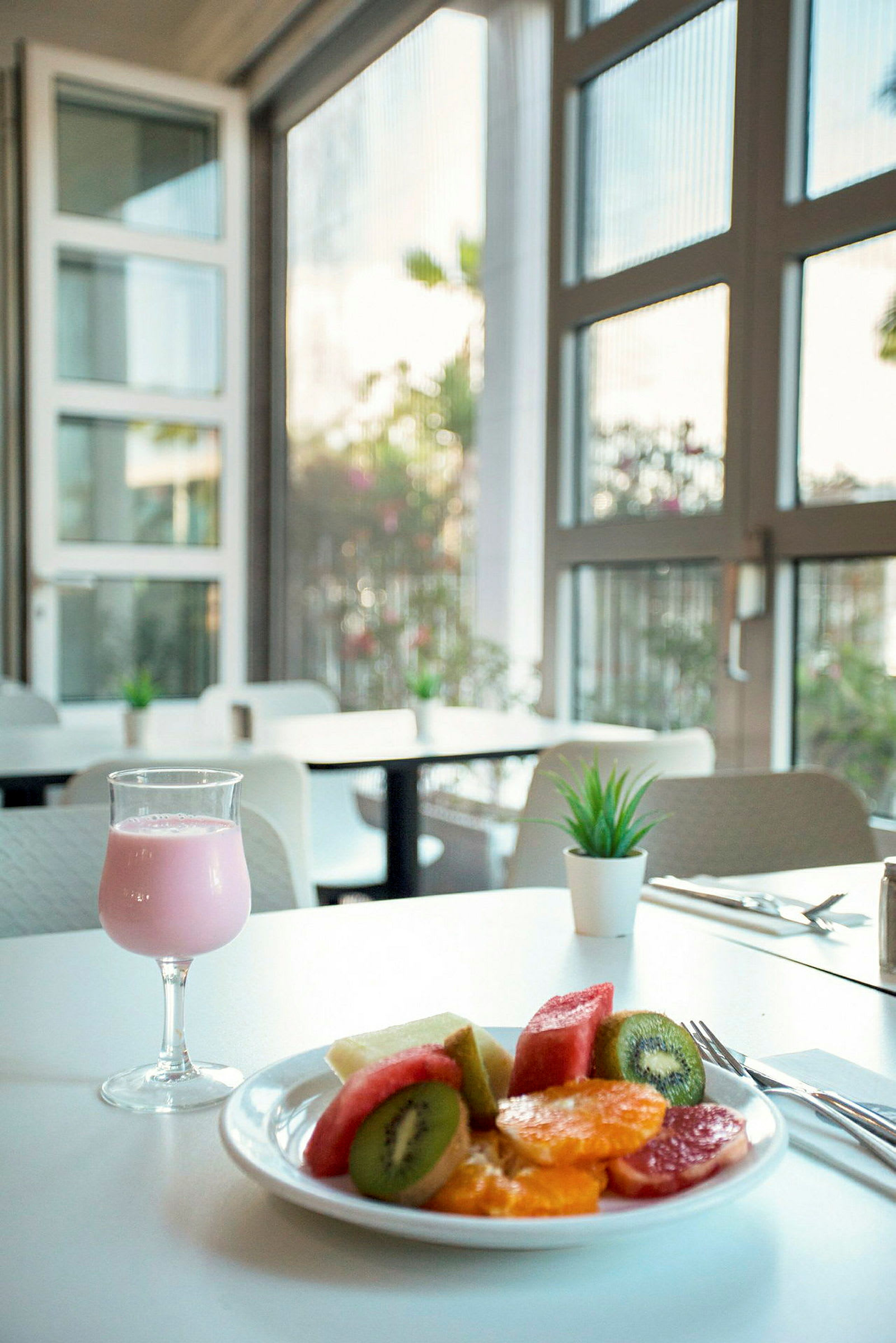 En tallrik med färsk frukt och ett glas rosa dryck på ett bord. (AI-genererad text)