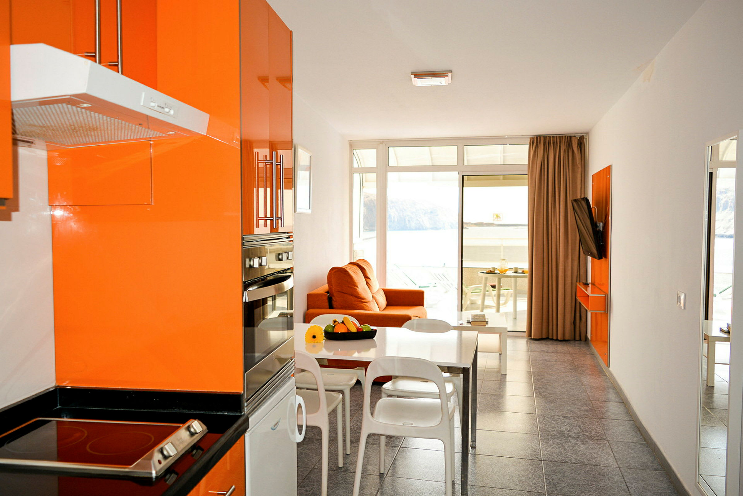 Modernt kök och vardagsrum med orange inredning och en utsikt mot havet. (AI-genererad text)