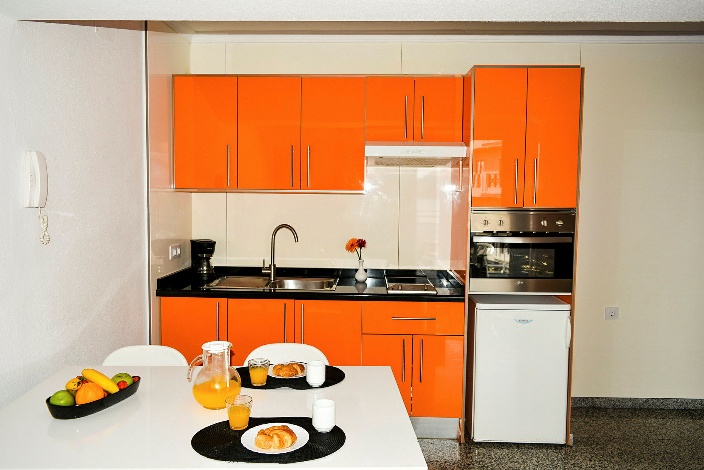 Kök med orange skåp, en matplats med frukost serverad, och vitvaror. (AI-genererad text)