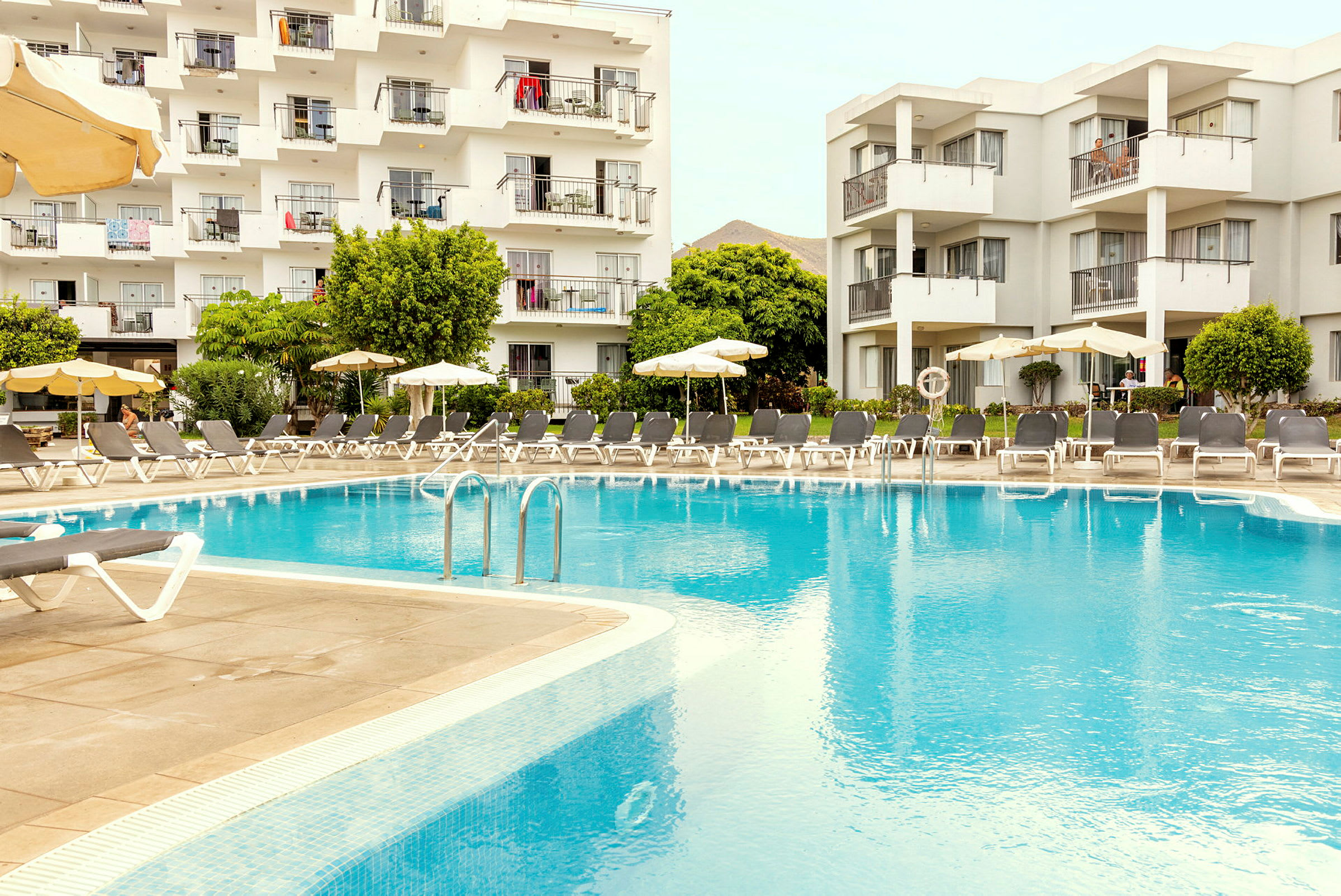 Hotellbyggnad med balkonger vid en stor utomhuspool. (AI-genererad text)