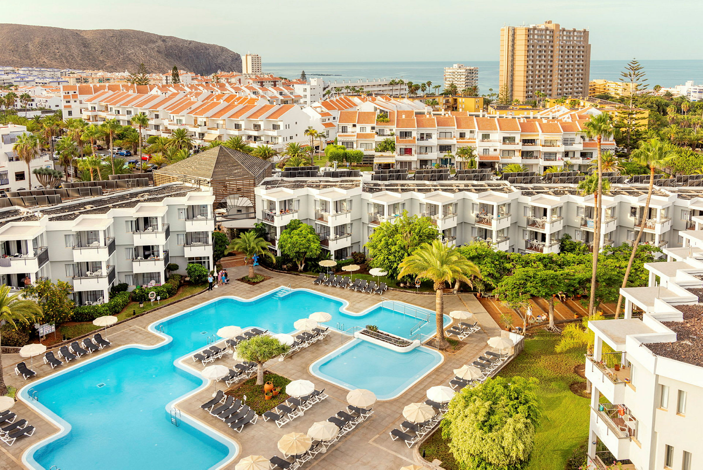 Vy över hotellområde med pooler, byggnader och omgivande landskap. (AI-genererad text)