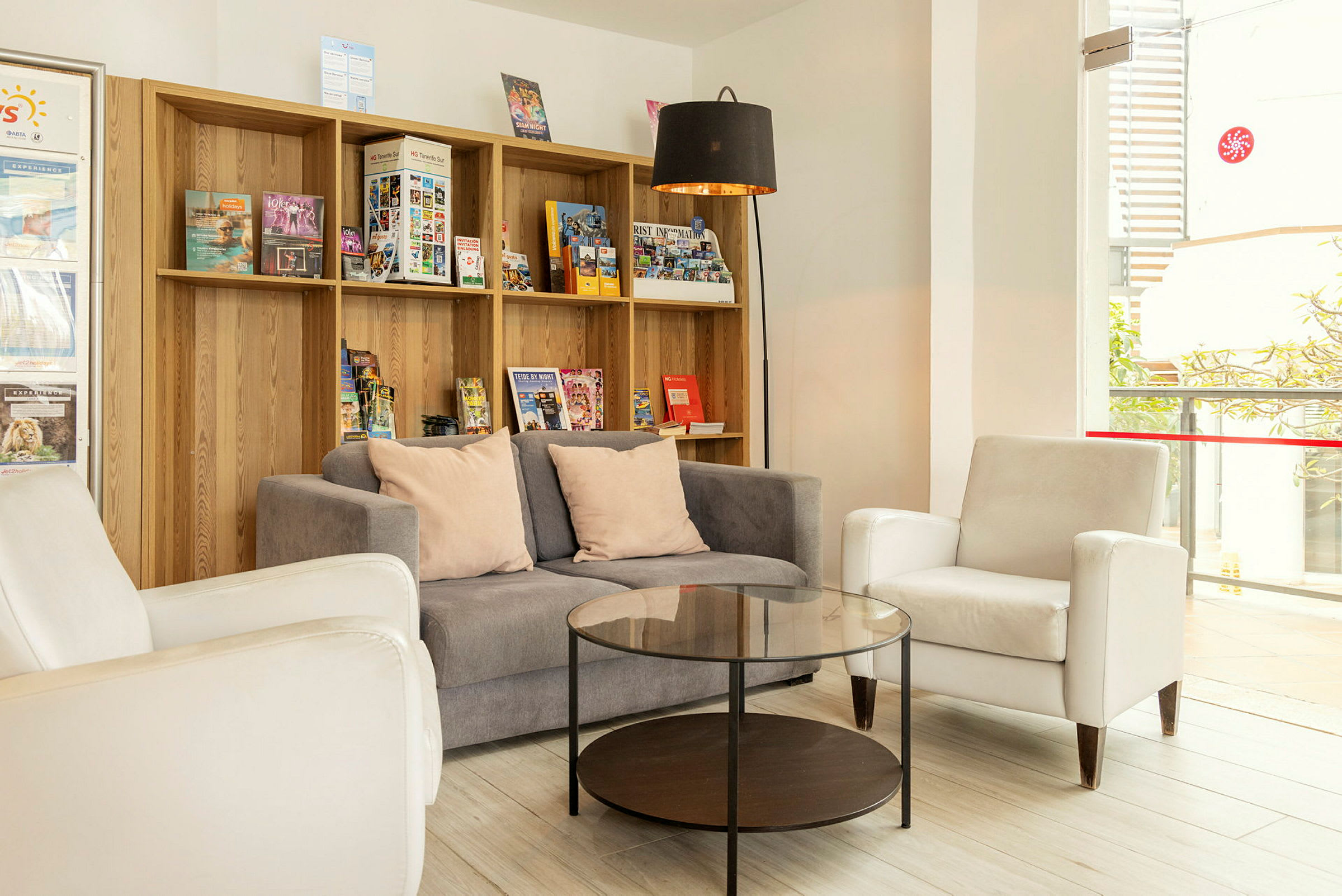 En lounge med soffa, fåtöljer och ett soffbord framför en hylla fylld med broschyrer. (AI-genererad text)