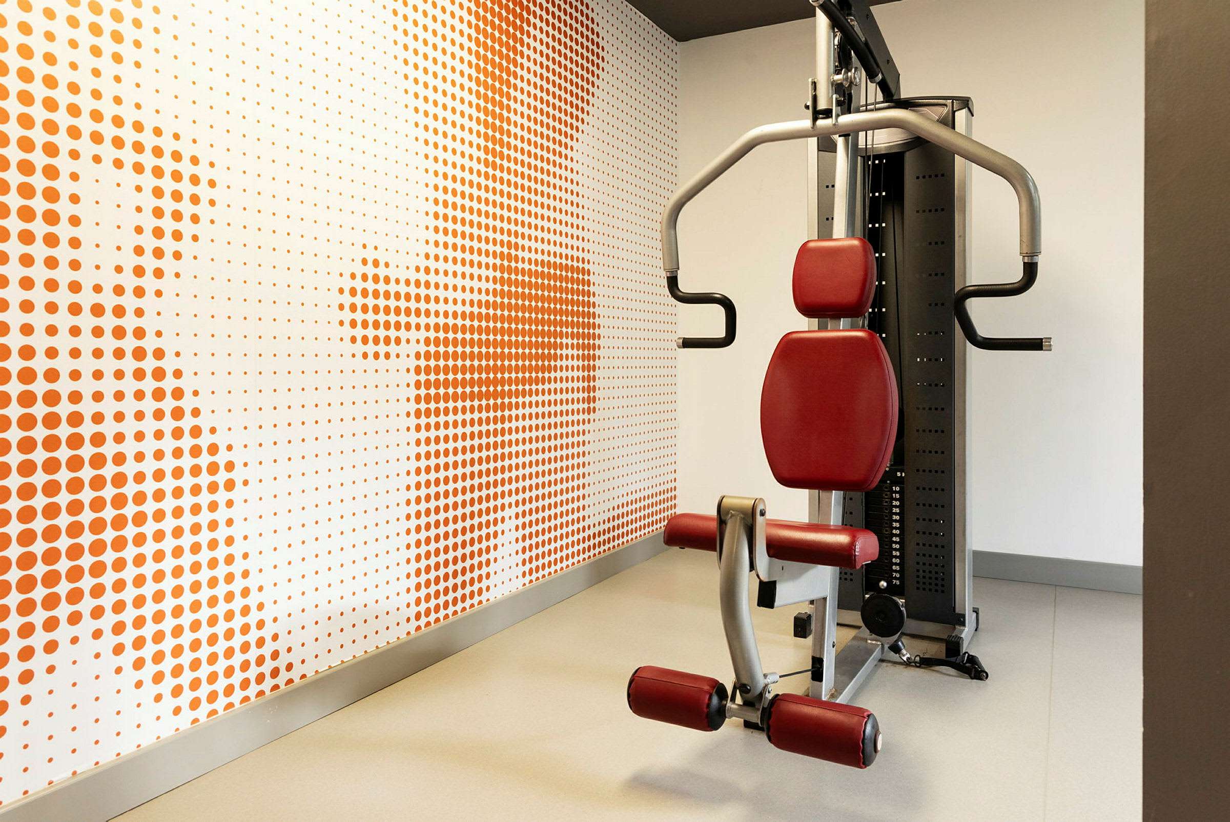 Träningsmaskin i ett gym, med en bakgrund av väggdekoration med orange prickar. (AI-genererad text)