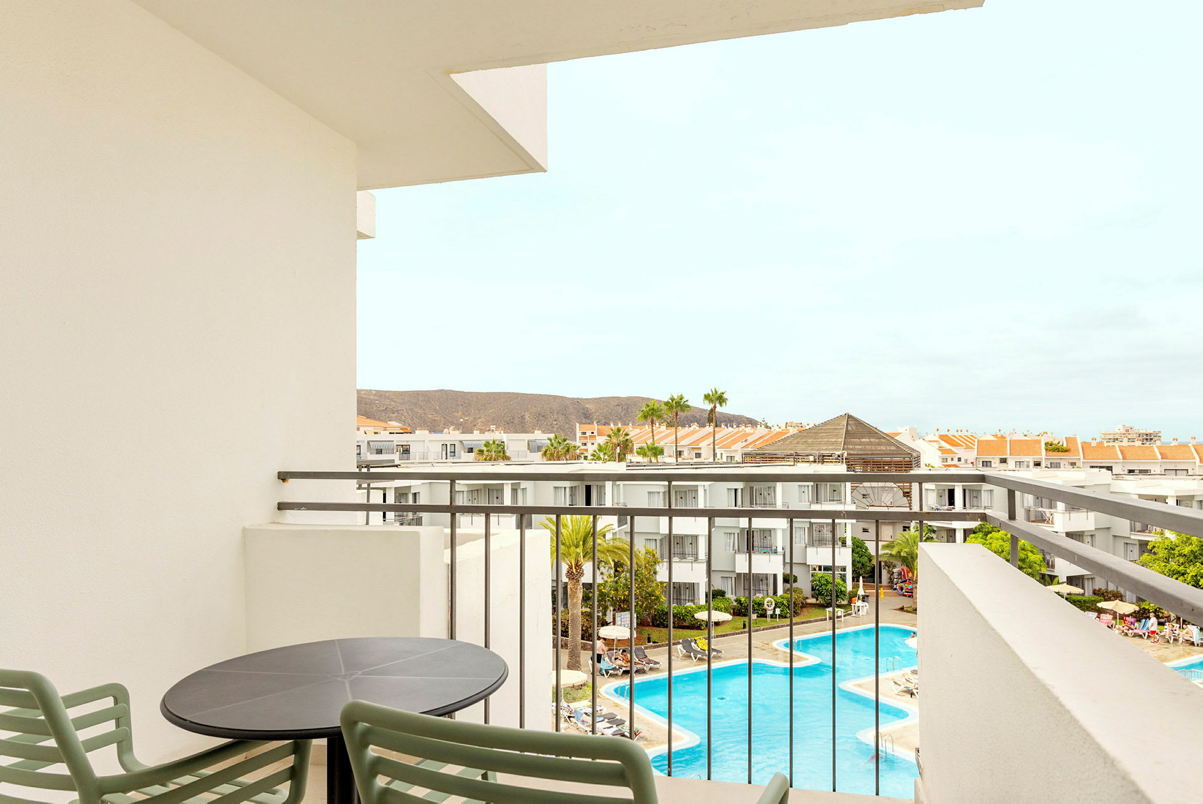 Utsikt från en balkong över hotellområdet med pool och omgivande byggnader. (AI-genererad text)