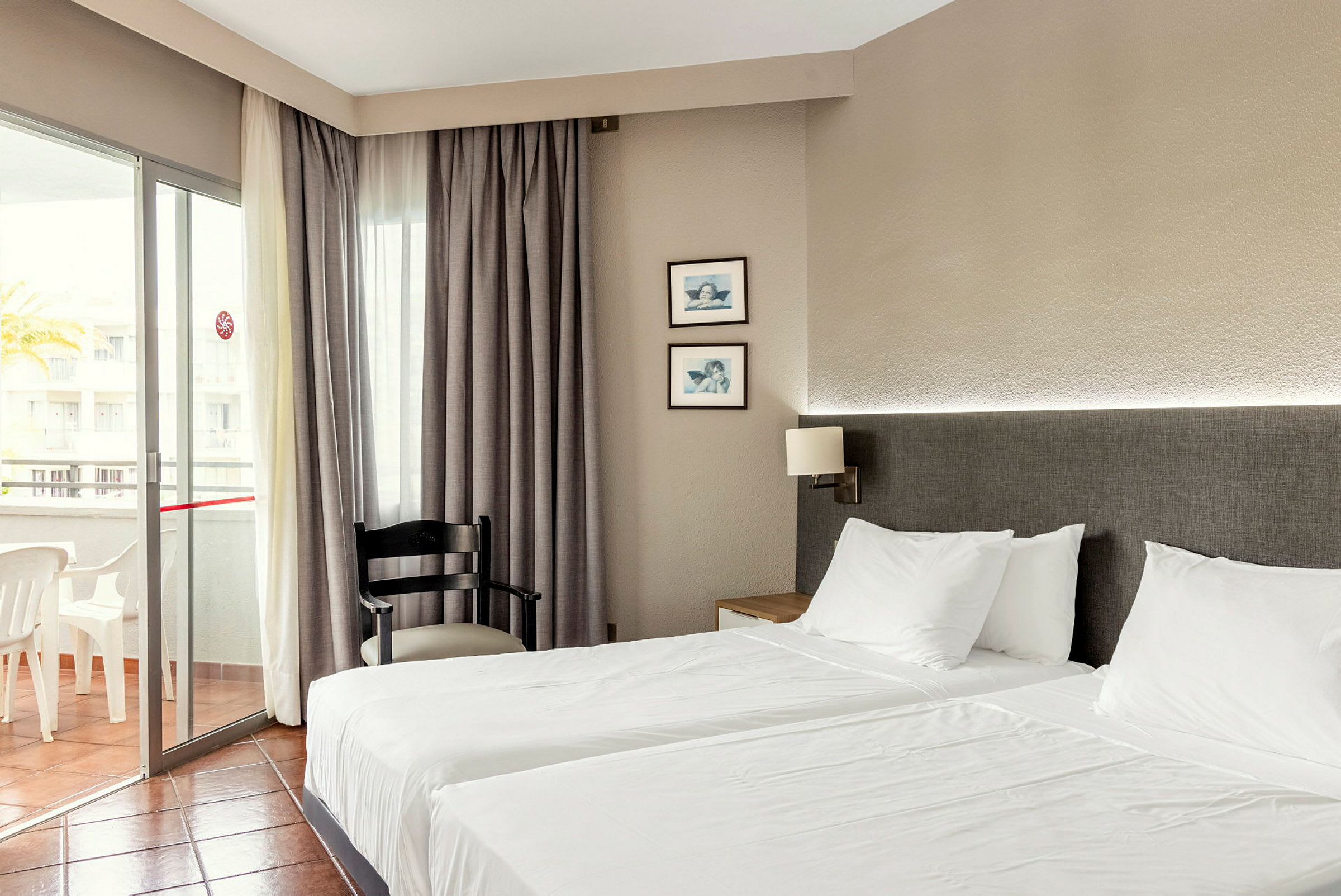 Hotellrum med två enkelsängar, en stol och en balkong. (AI-genererad text)
