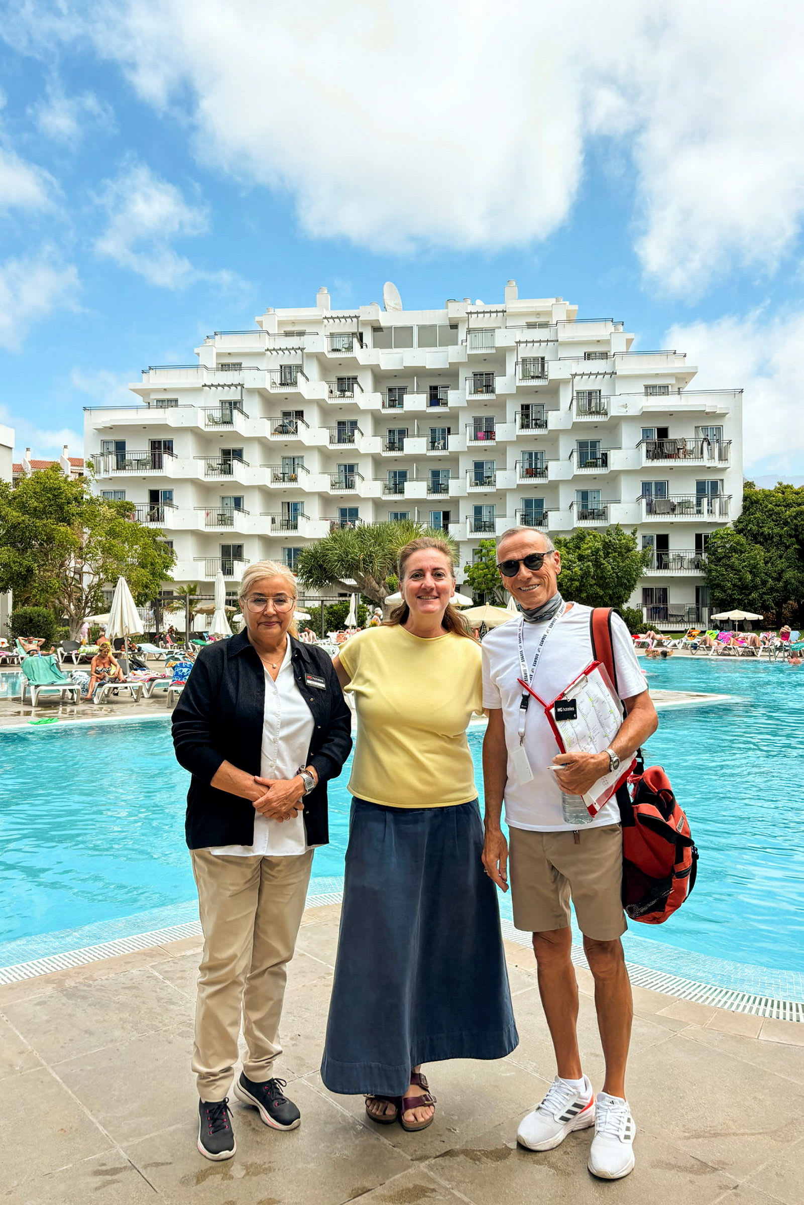 Hotellbyggnad vid en utomhuspool med människor och solstolar. (AI-genererad text)