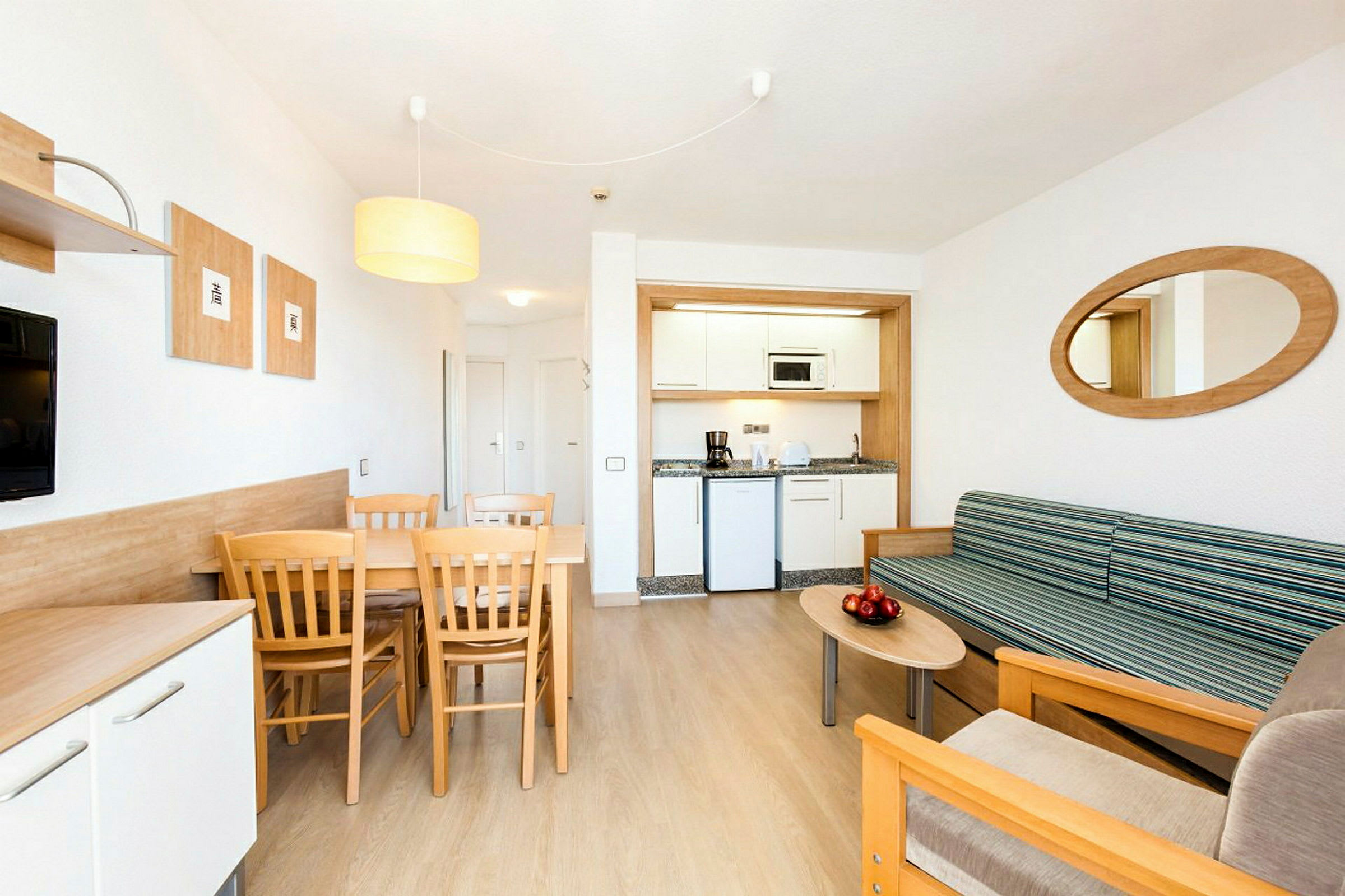 En modern hotellrum med ett litet köksutrymme, en matplats med bord och stolar samt en sittgrupp med soffa och soffbord. (AI-genererad text)